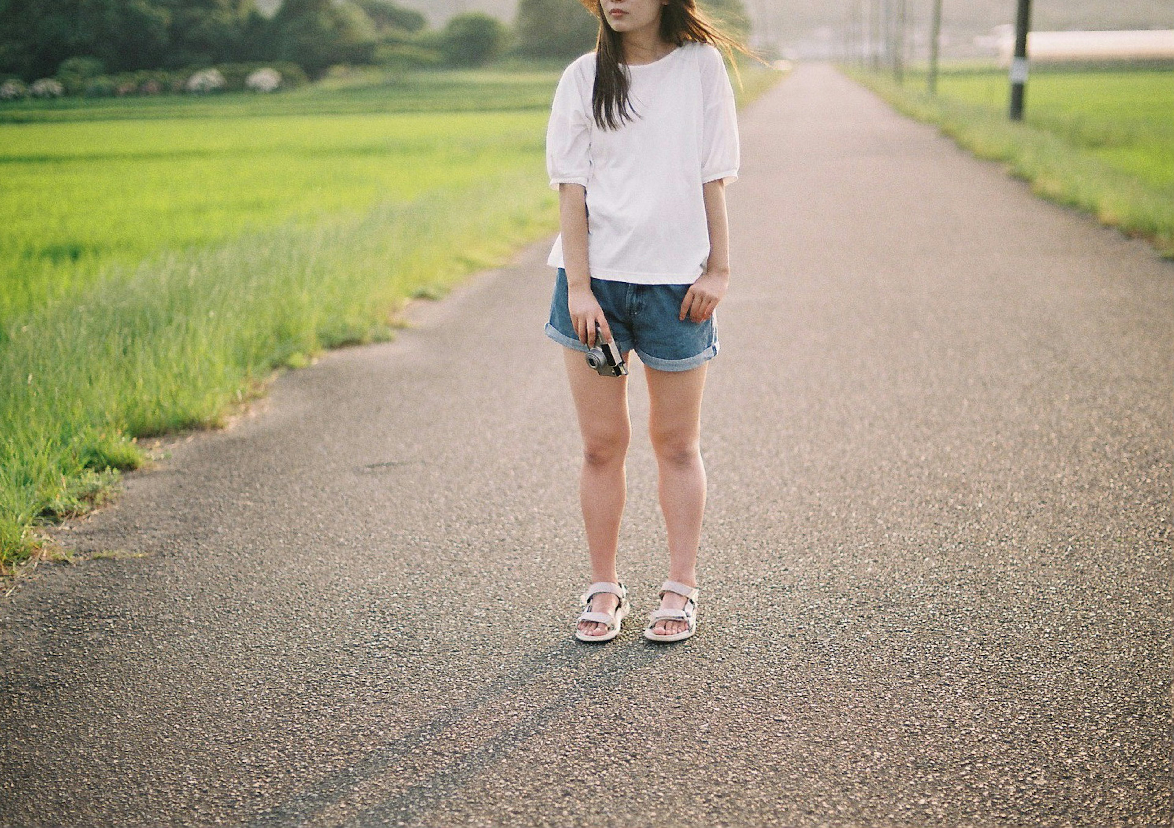 Une femme portant un t-shirt blanc et un short en denim se tenant sur une route rurale