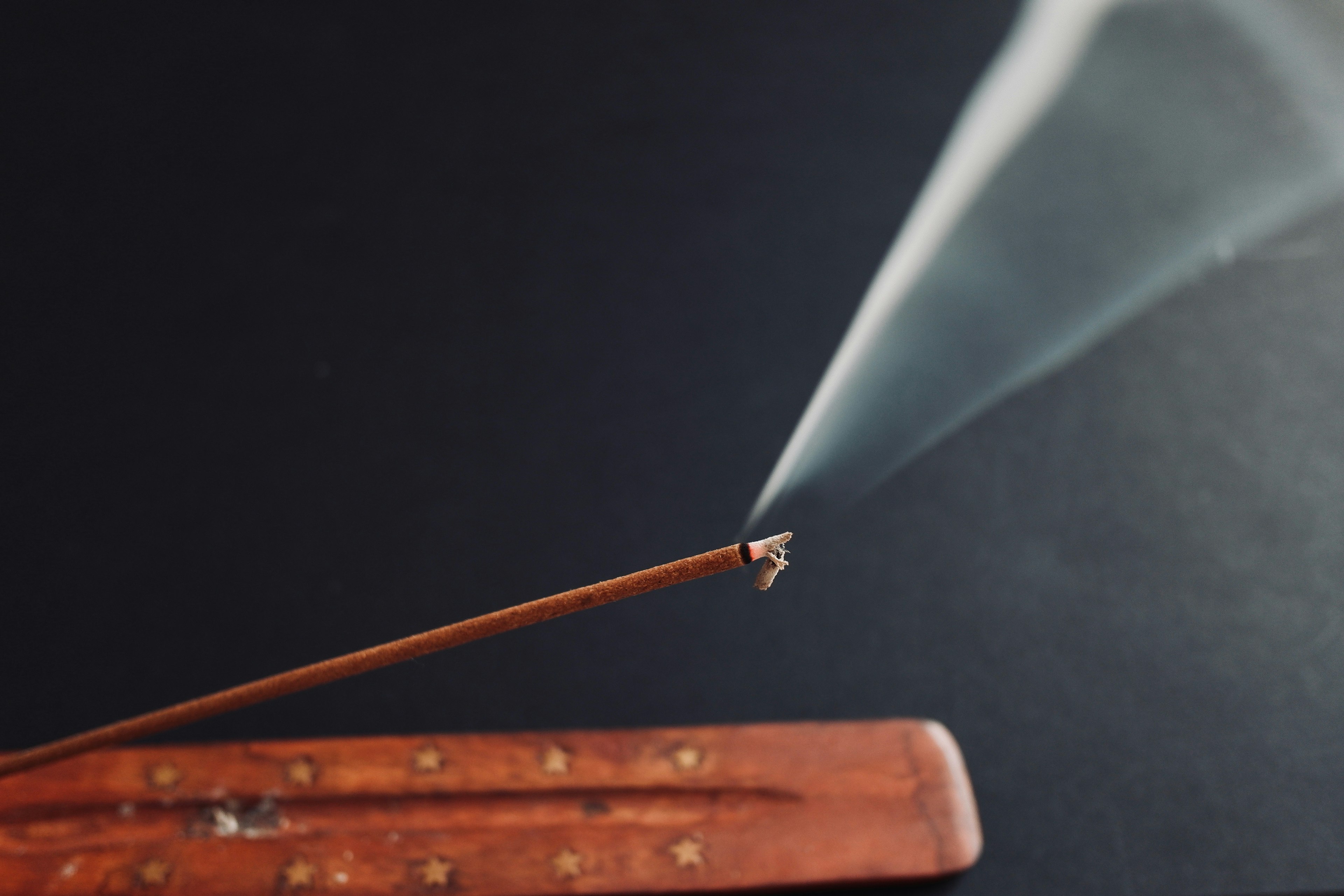 Close-up of incense stick emitting smoke with wooden holder