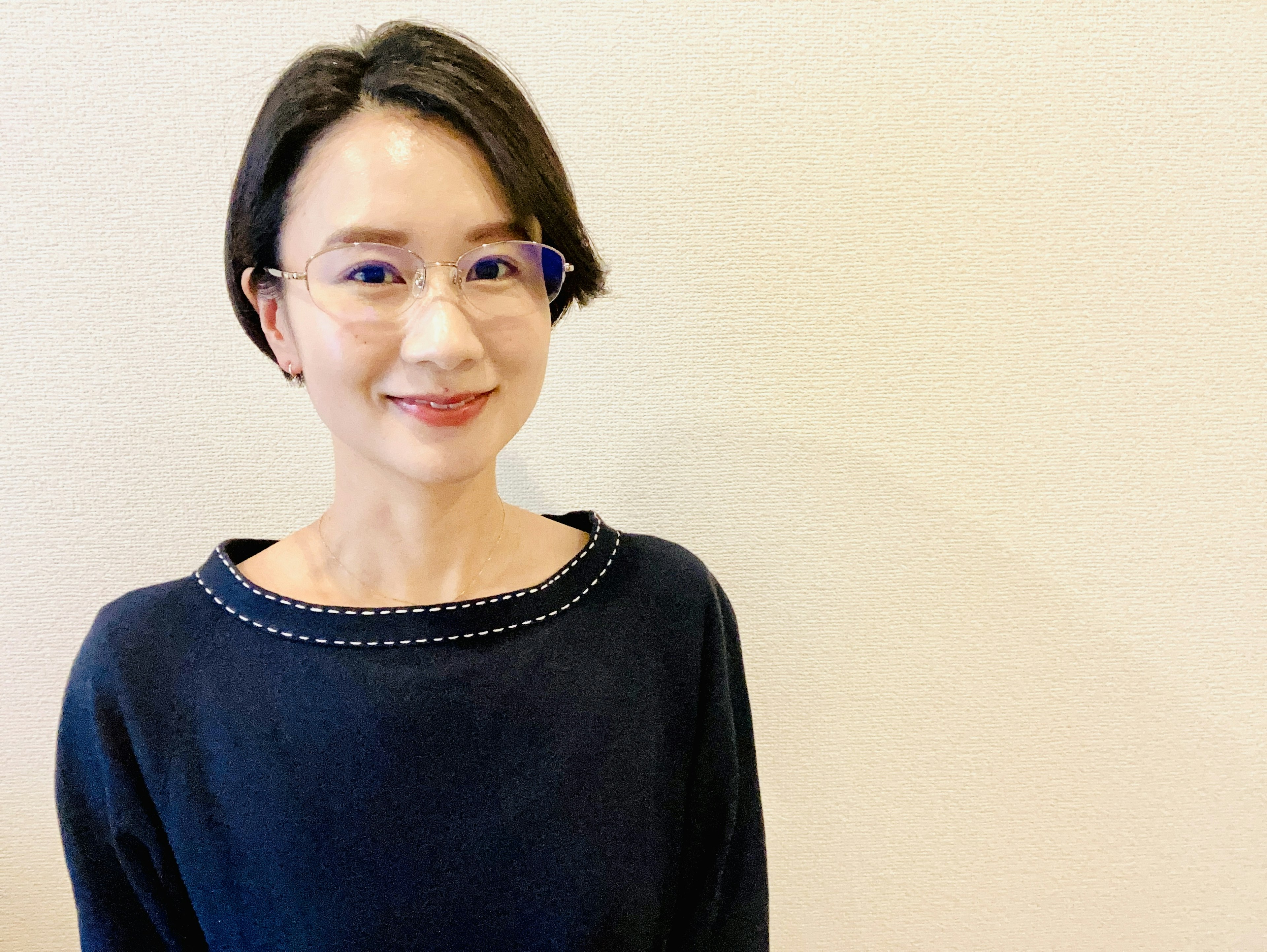 A woman in a blue sweater smiles against a light-colored background