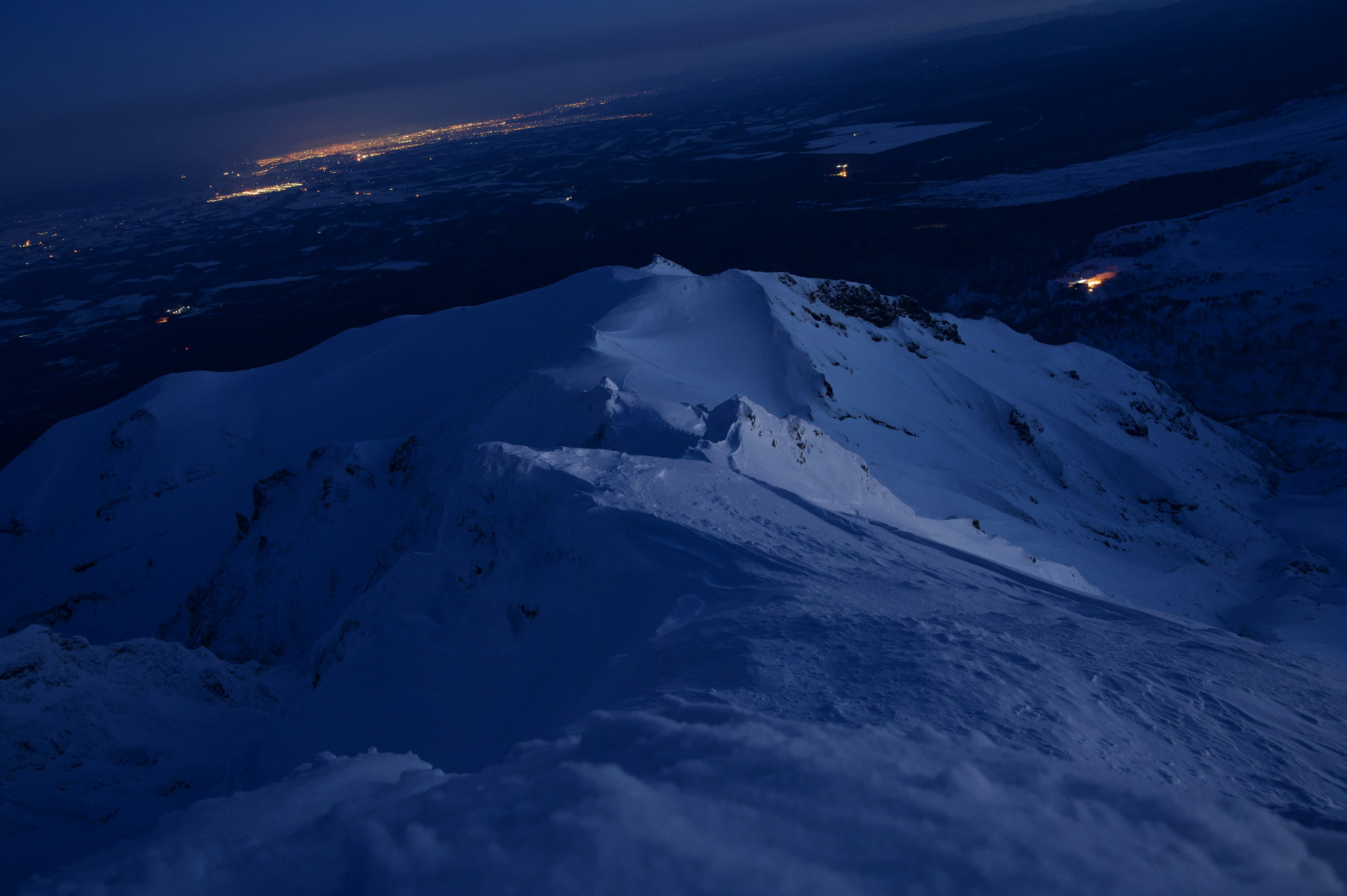 夜の山の頂上に雪が覆われた風景と遠くの街の明かり