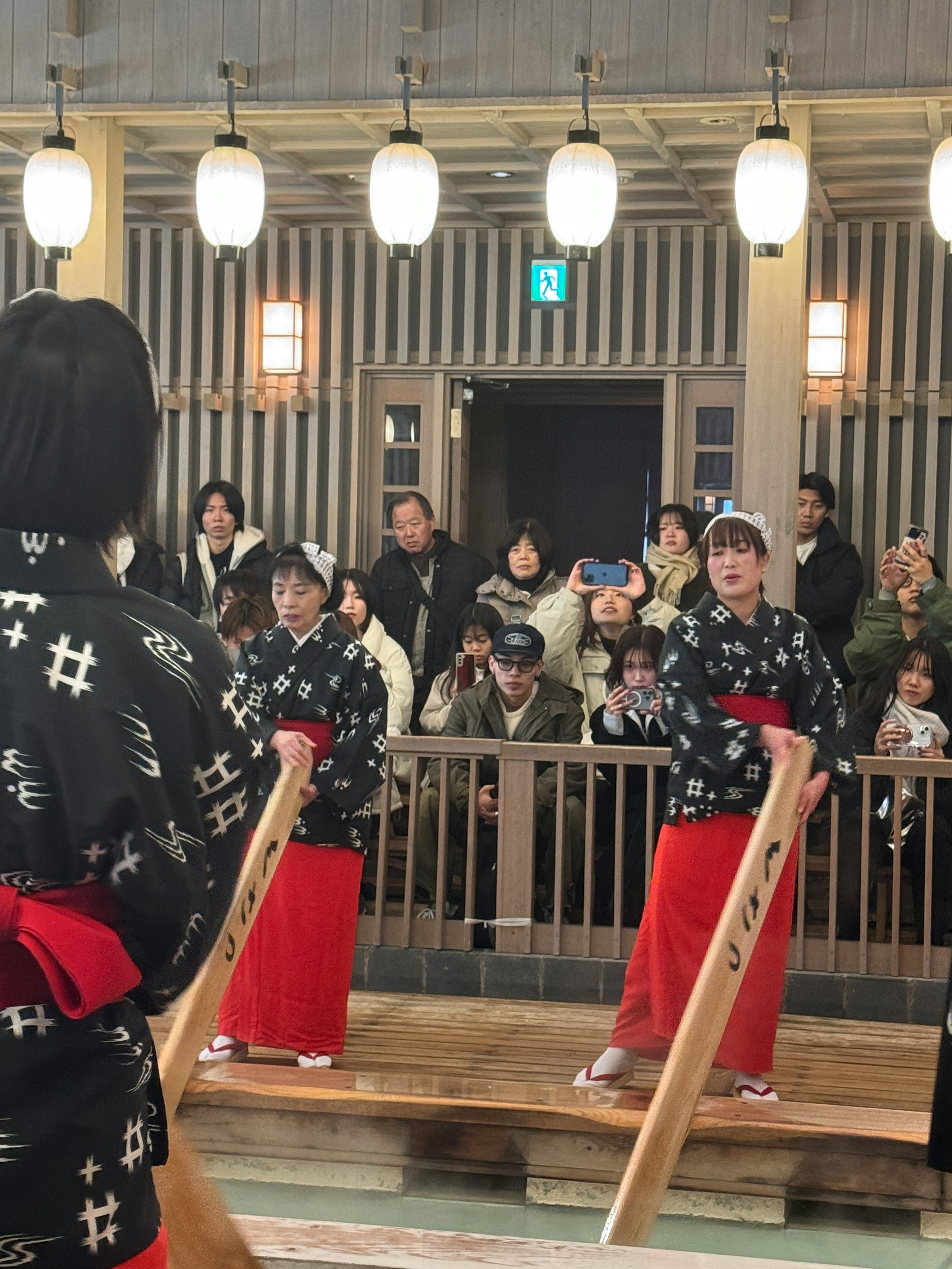 Women in traditional attire holding wooden sticks standing in front of an audience