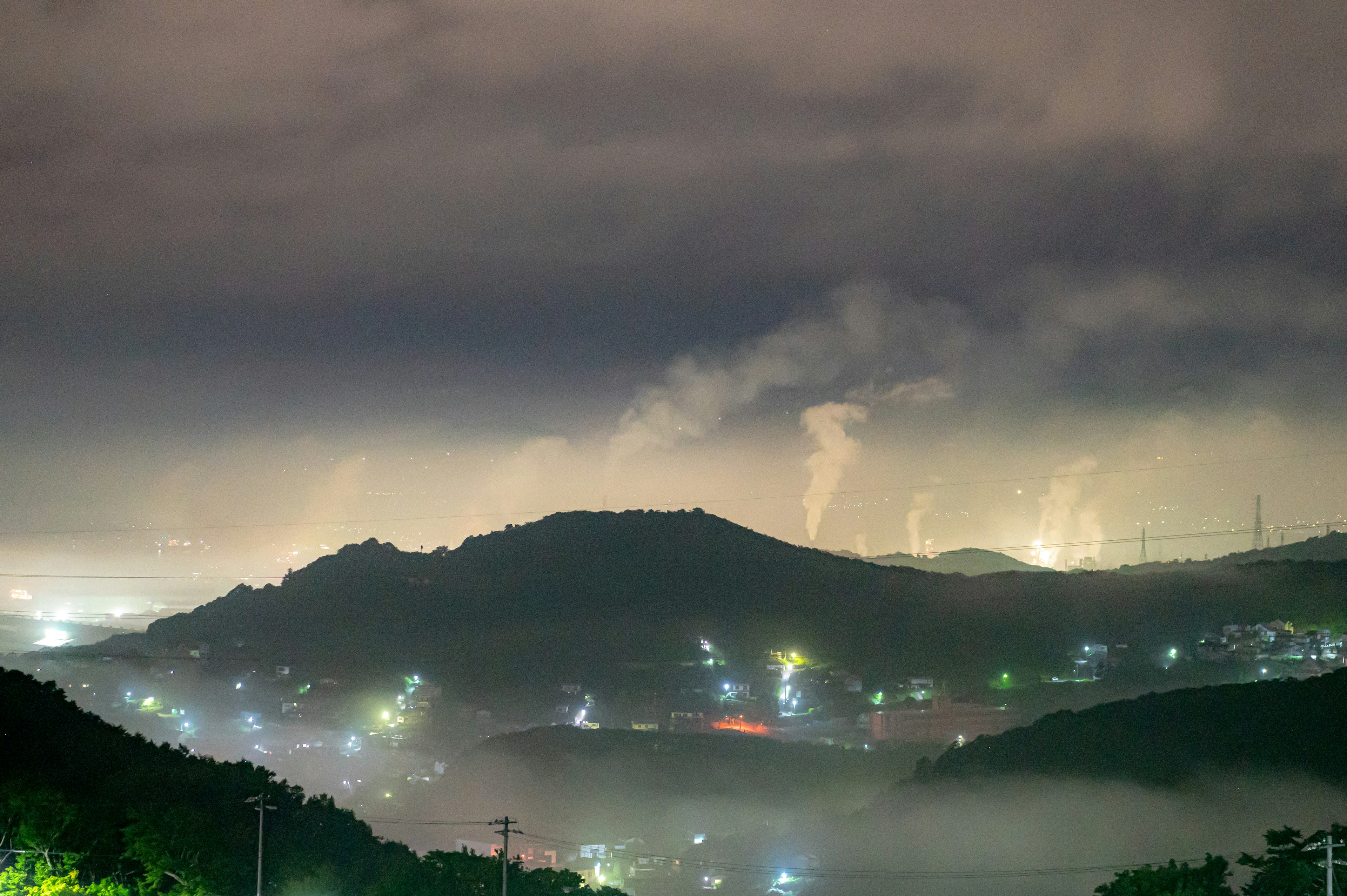 Foggy mountains under a night sky with factory smoke