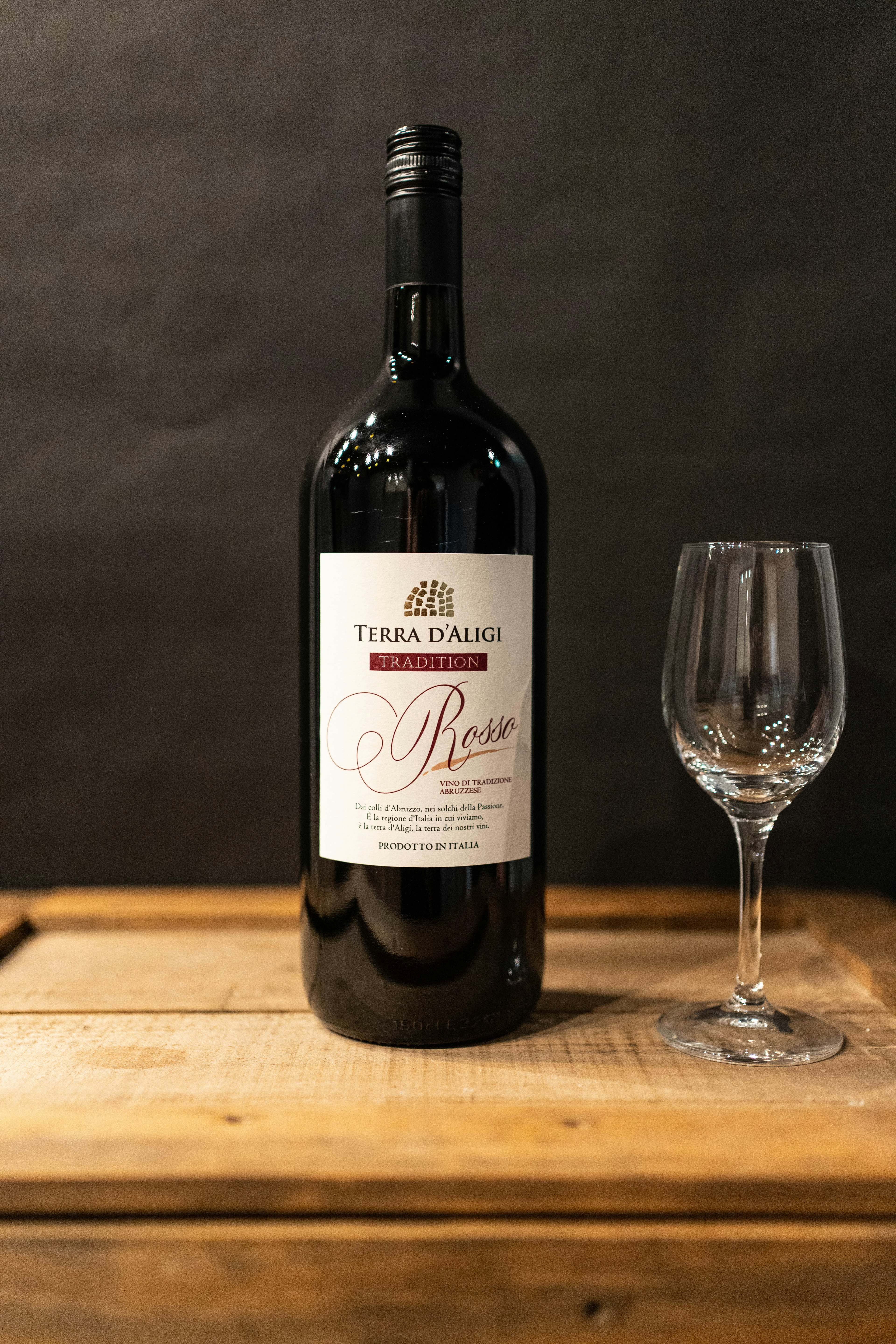 A red wine bottle and an empty wine glass placed on a wooden table