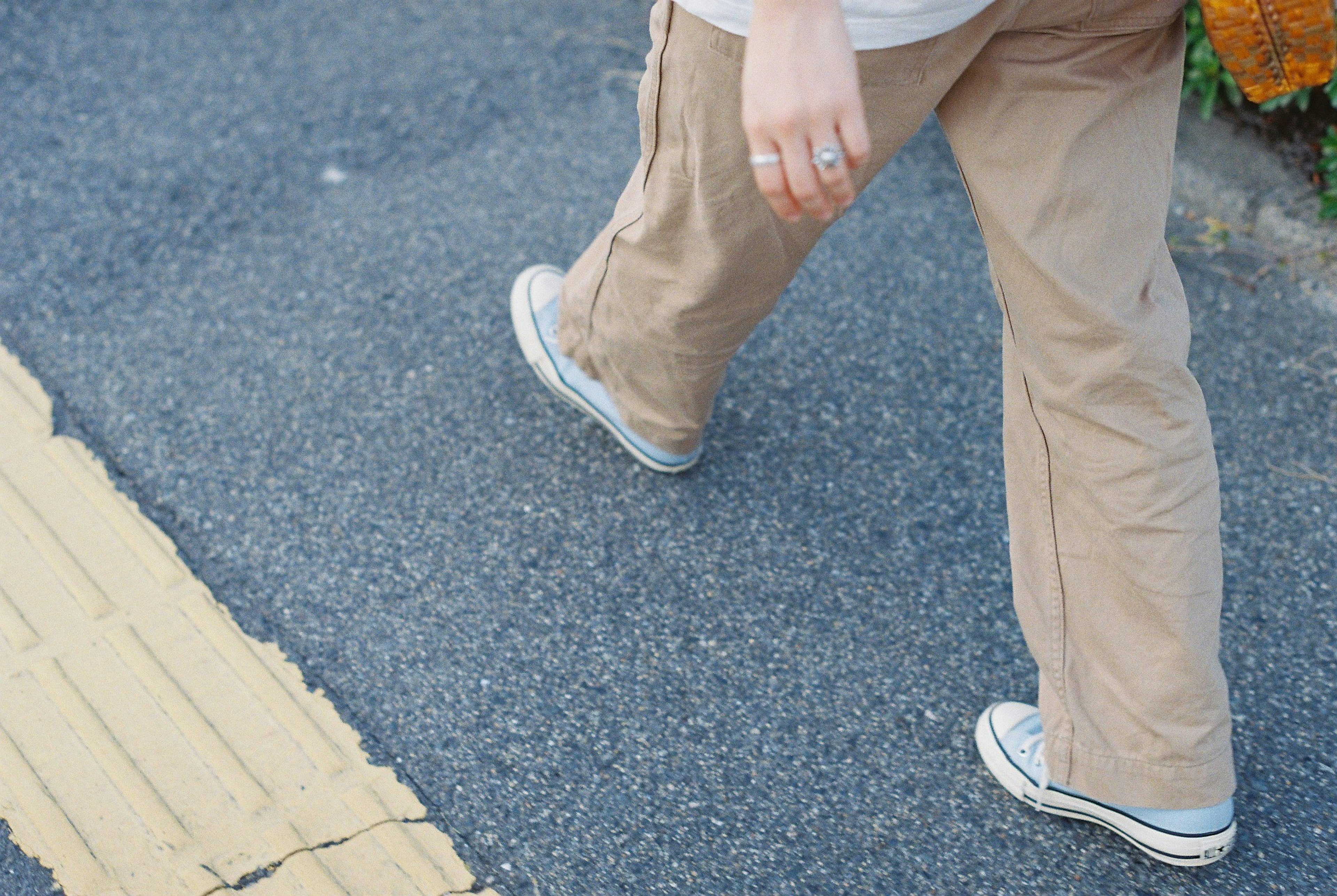 Gambar close-up kaki seseorang yang berjalan di atas trotoar mengenakan celana berwarna terang dan sepatu sneakers