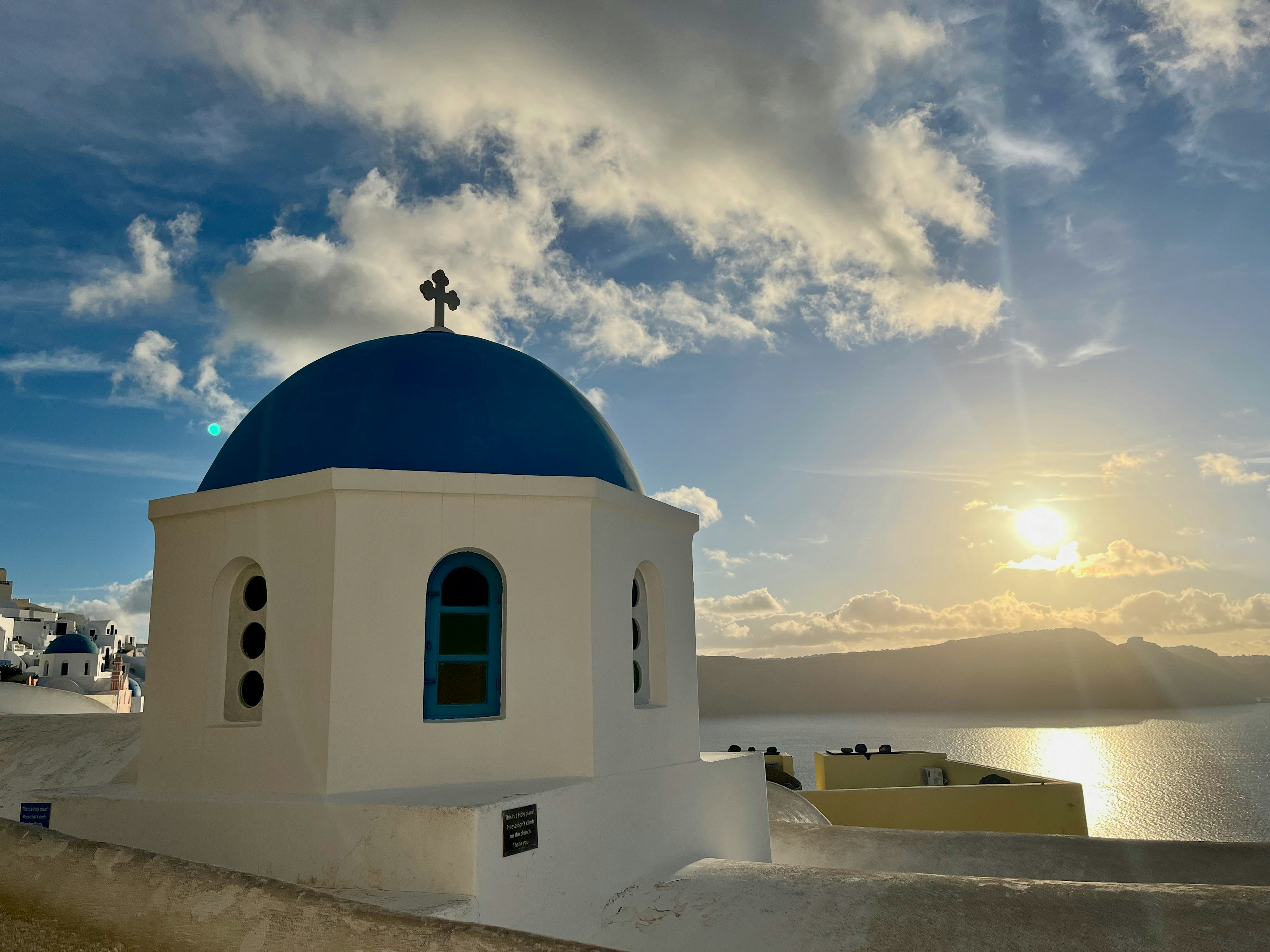 Iglesia blanca con cúpula azul y cruz al atardecer