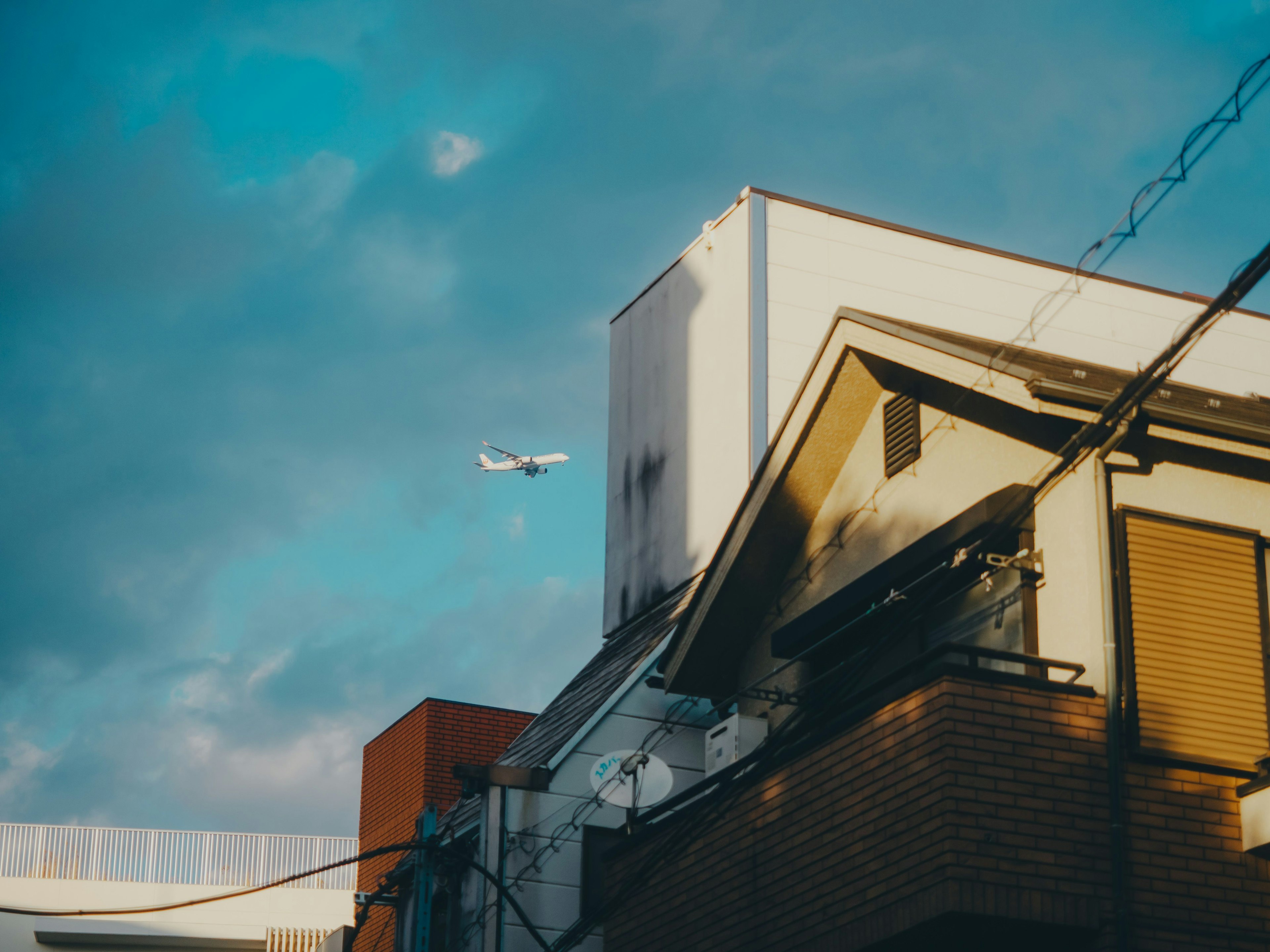 Foto eines Flugzeugs, das über einem Haus unter einem blauen Himmel fliegt