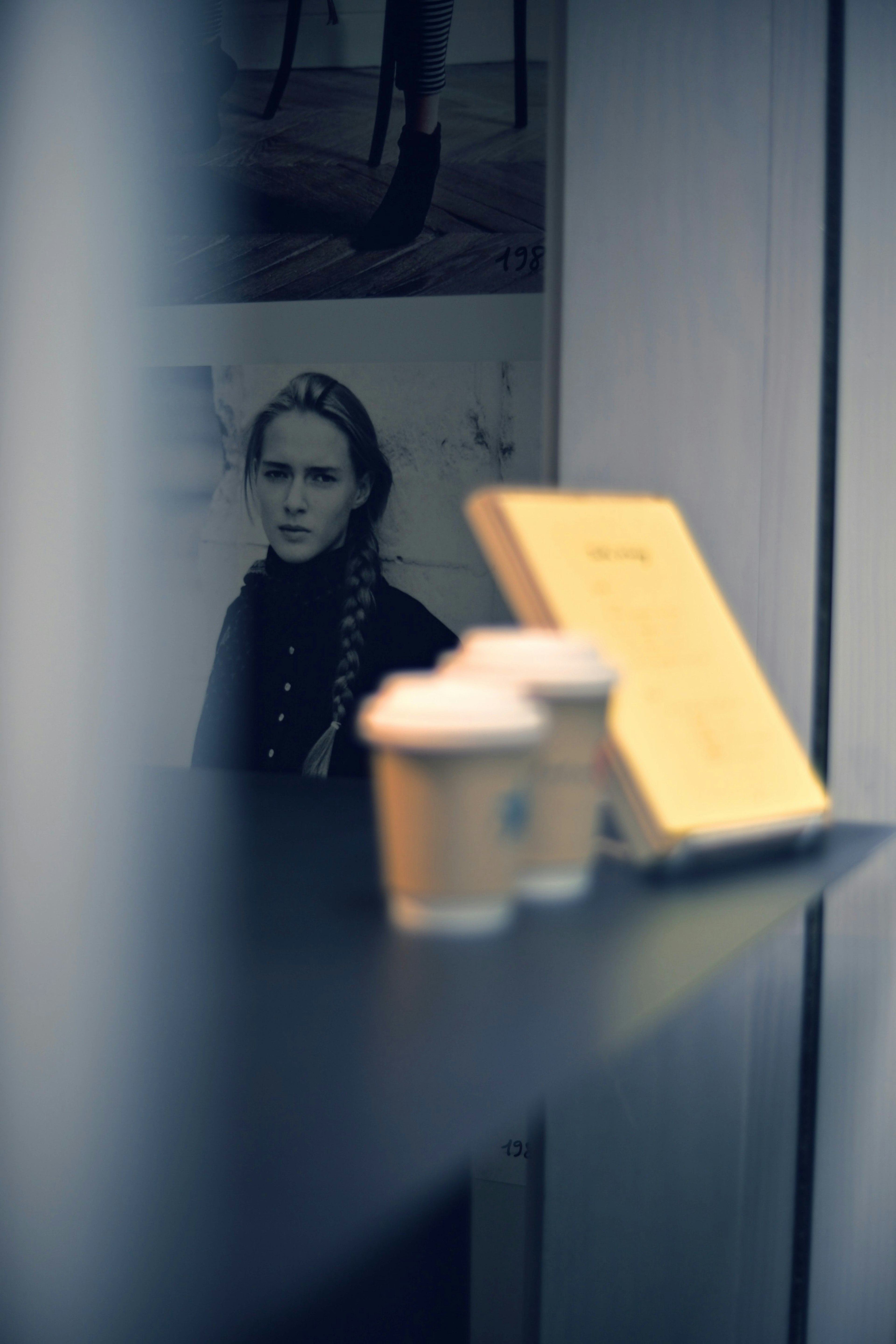 Coffee cups and a yellow book on a cafe table with a portrait of a woman in the background