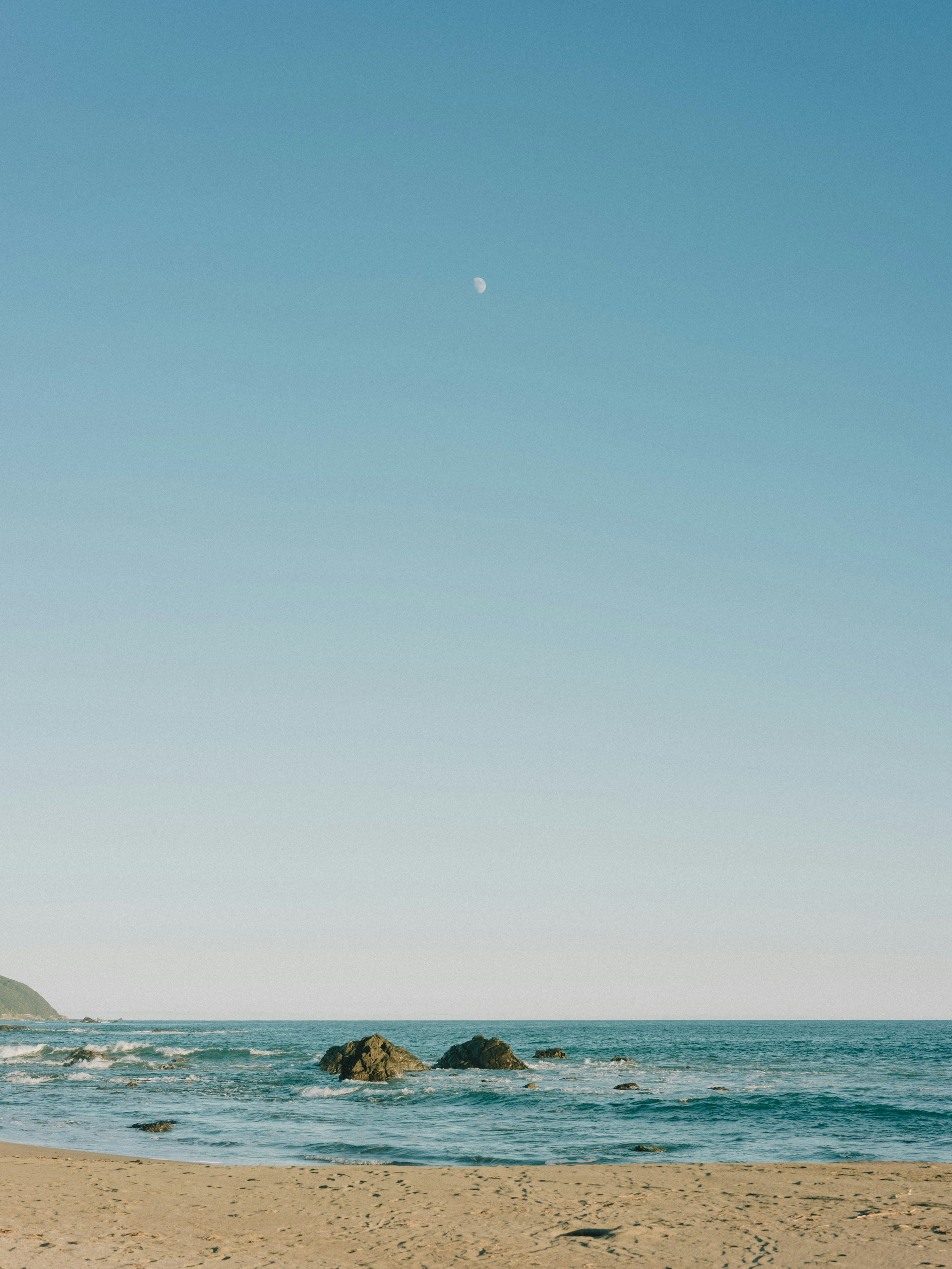 Escena de playa serena con cielo azul y océano Luna visible en el cielo