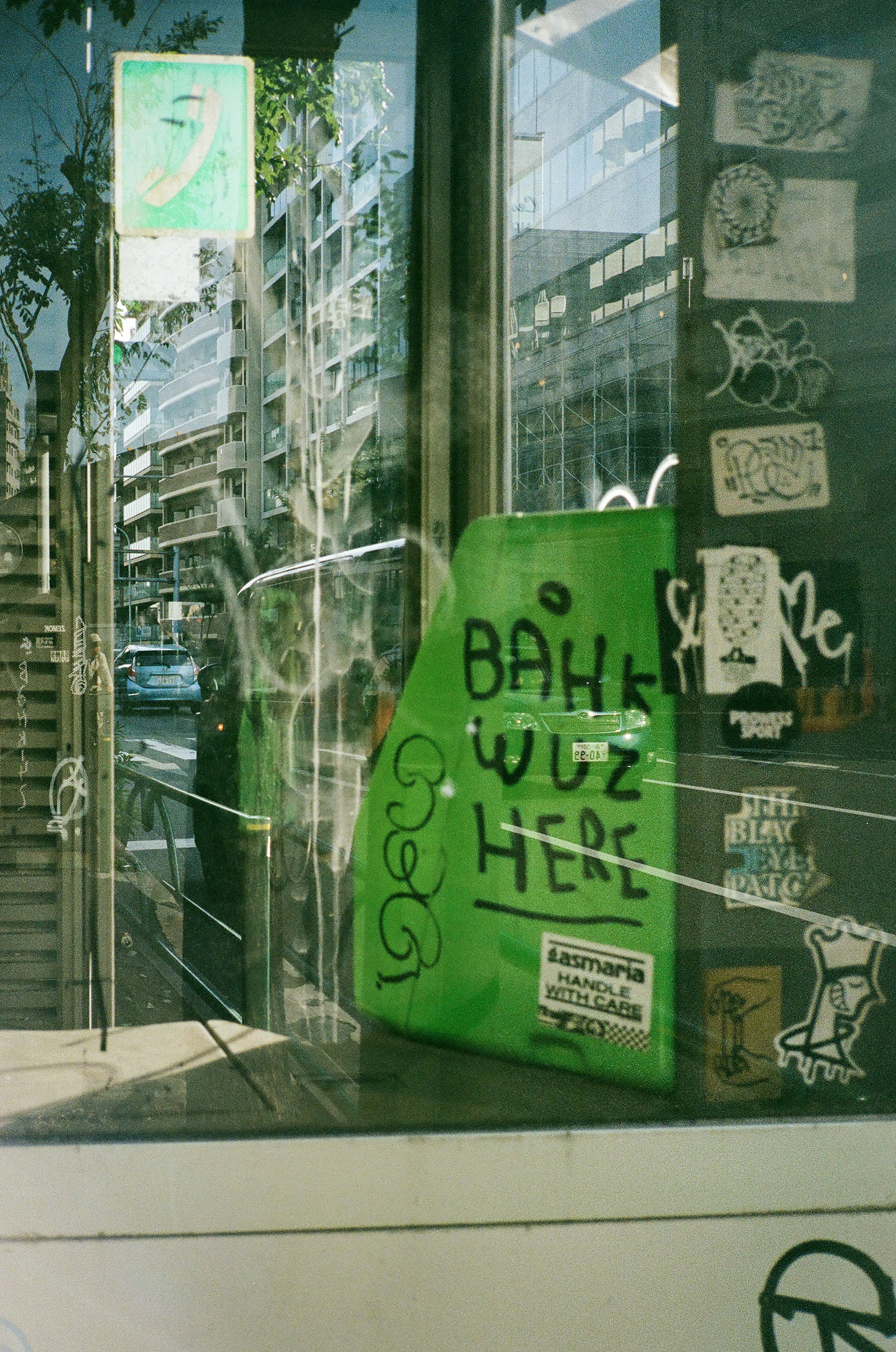 Grünes Schild mit dem Text "BAHK WUZ HERE" sichtbar durch ein Schaufenster im Straßenkunststil