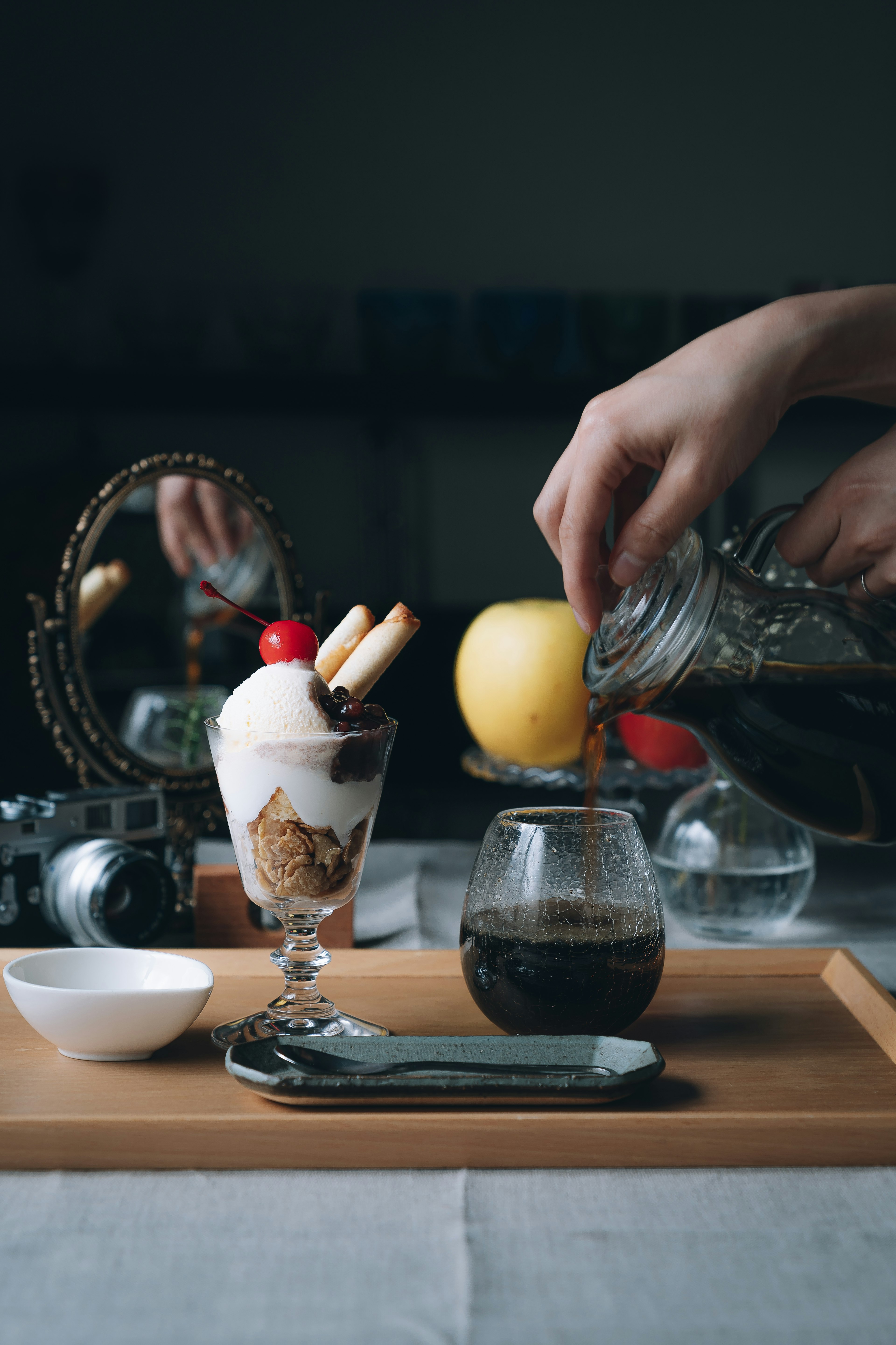 Scene featuring an ice cream parfait topped with cream and fruit on a wooden table