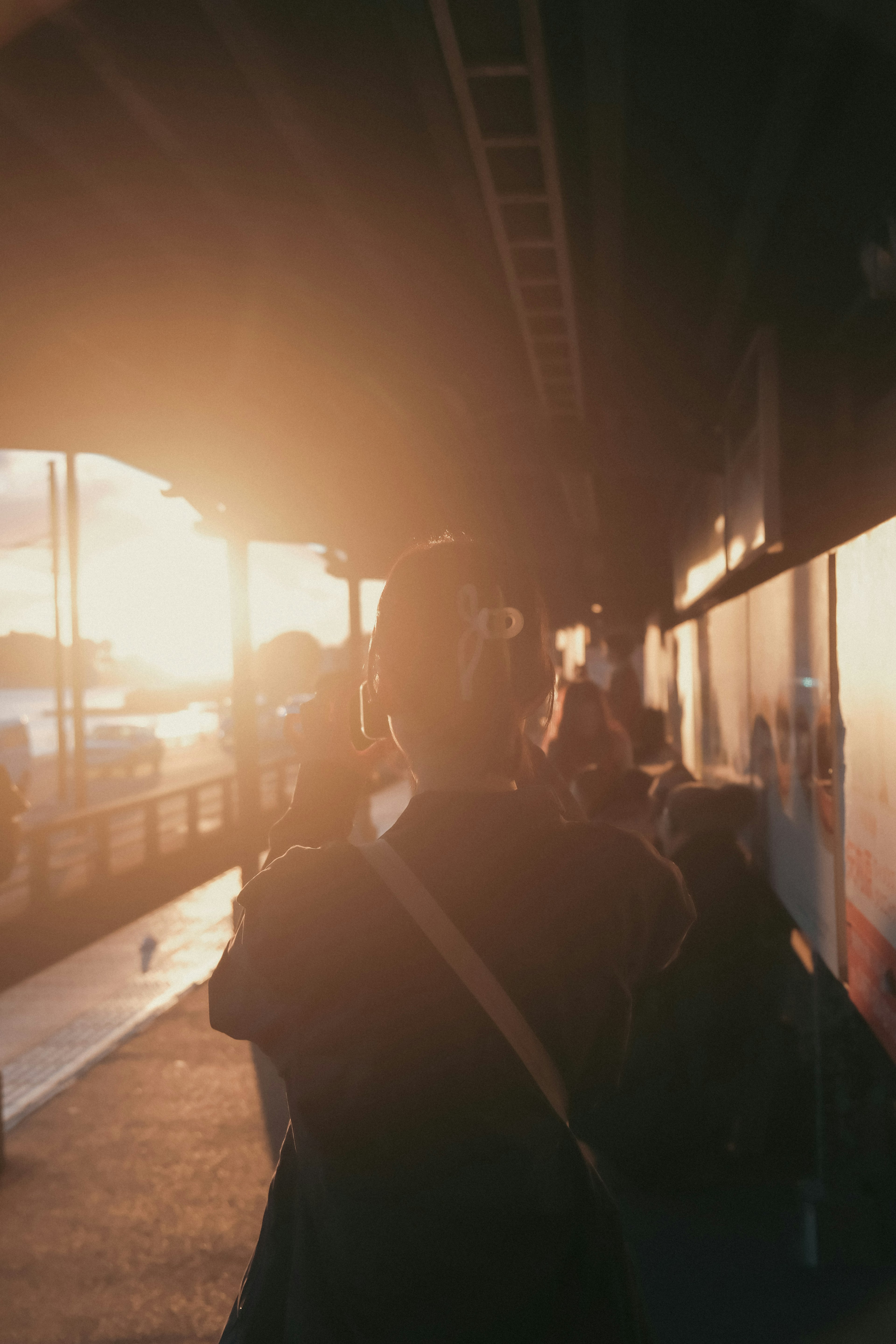 A person walking on a sidewalk with their back to the sunset and surrounded by other people