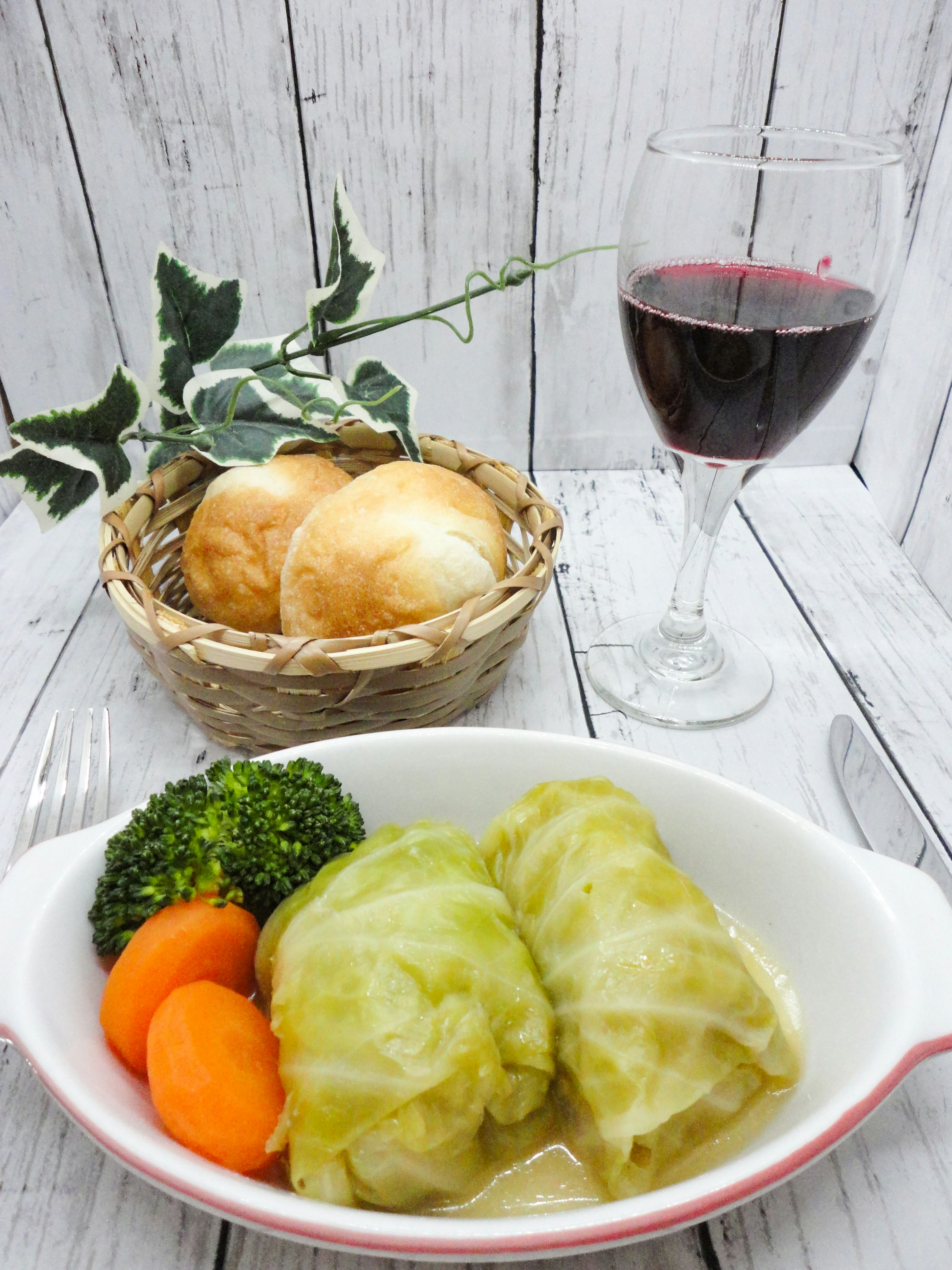 Kohlrouladen mit Brokkoli und Karotten, ein Korb mit Brot und ein Glas Rotwein