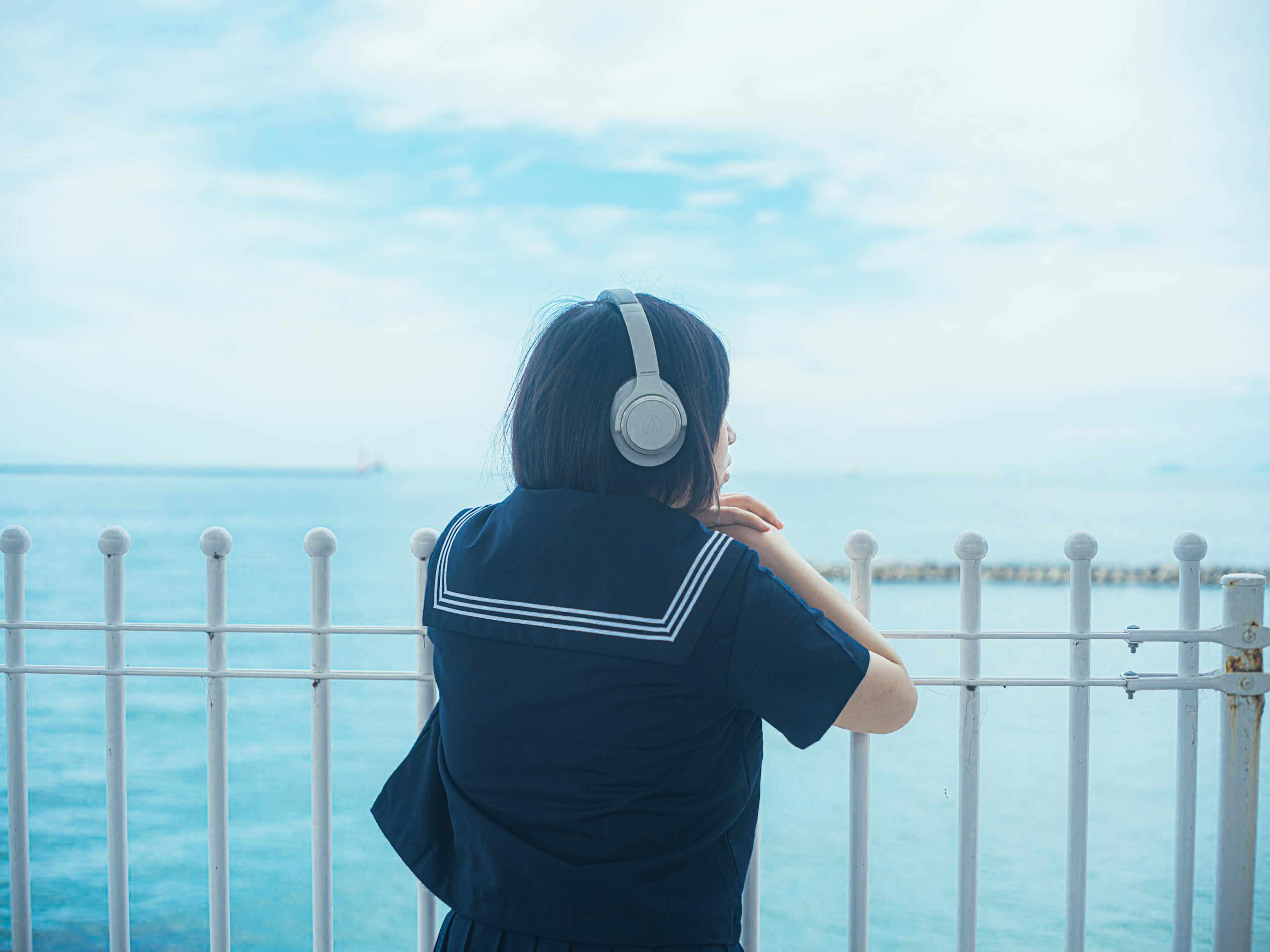 Une fille en uniforme scolaire portant des écouteurs regardant la mer bleue