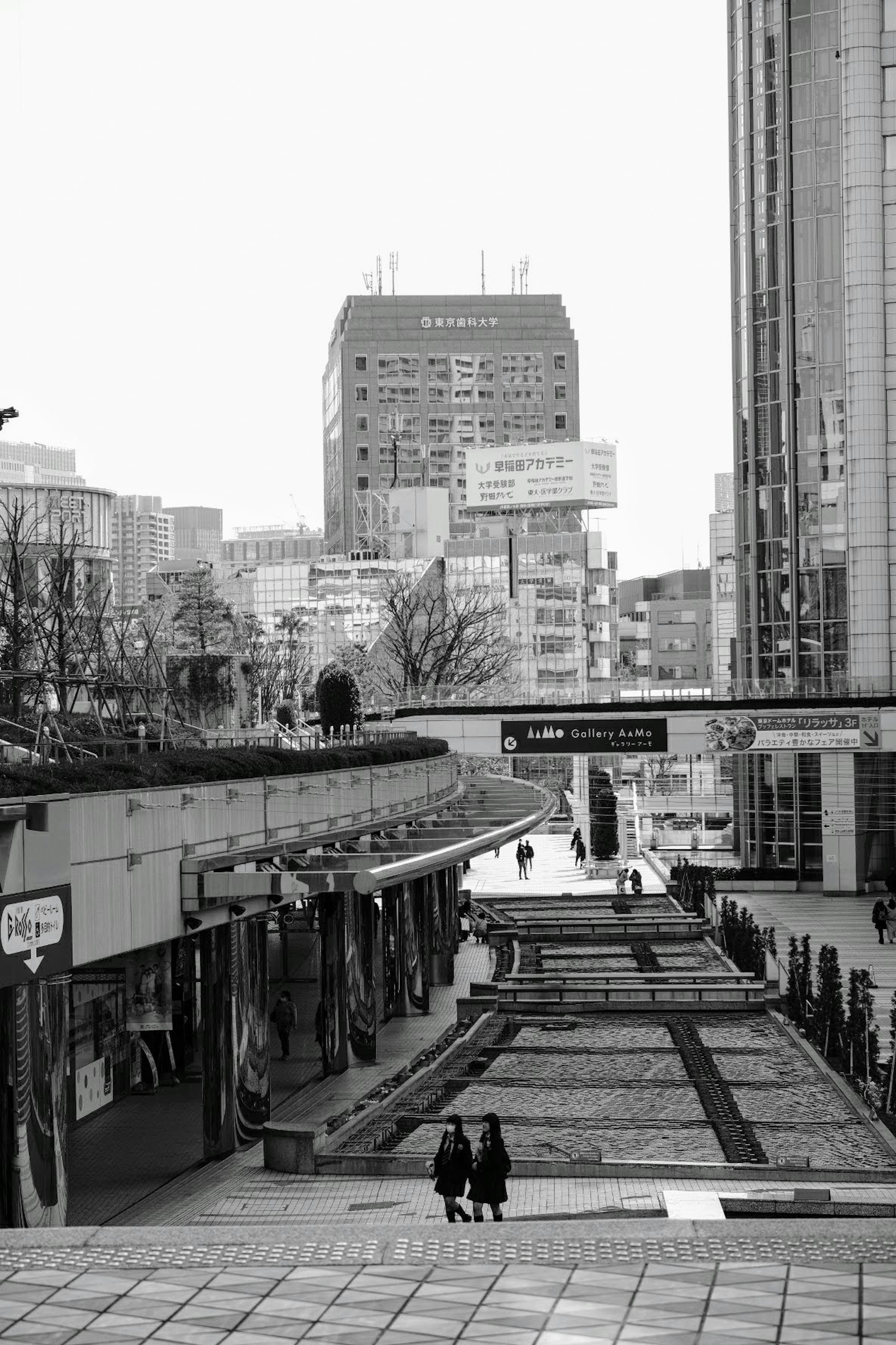 Black and white urban scene with people walking along a street and high-rise buildings