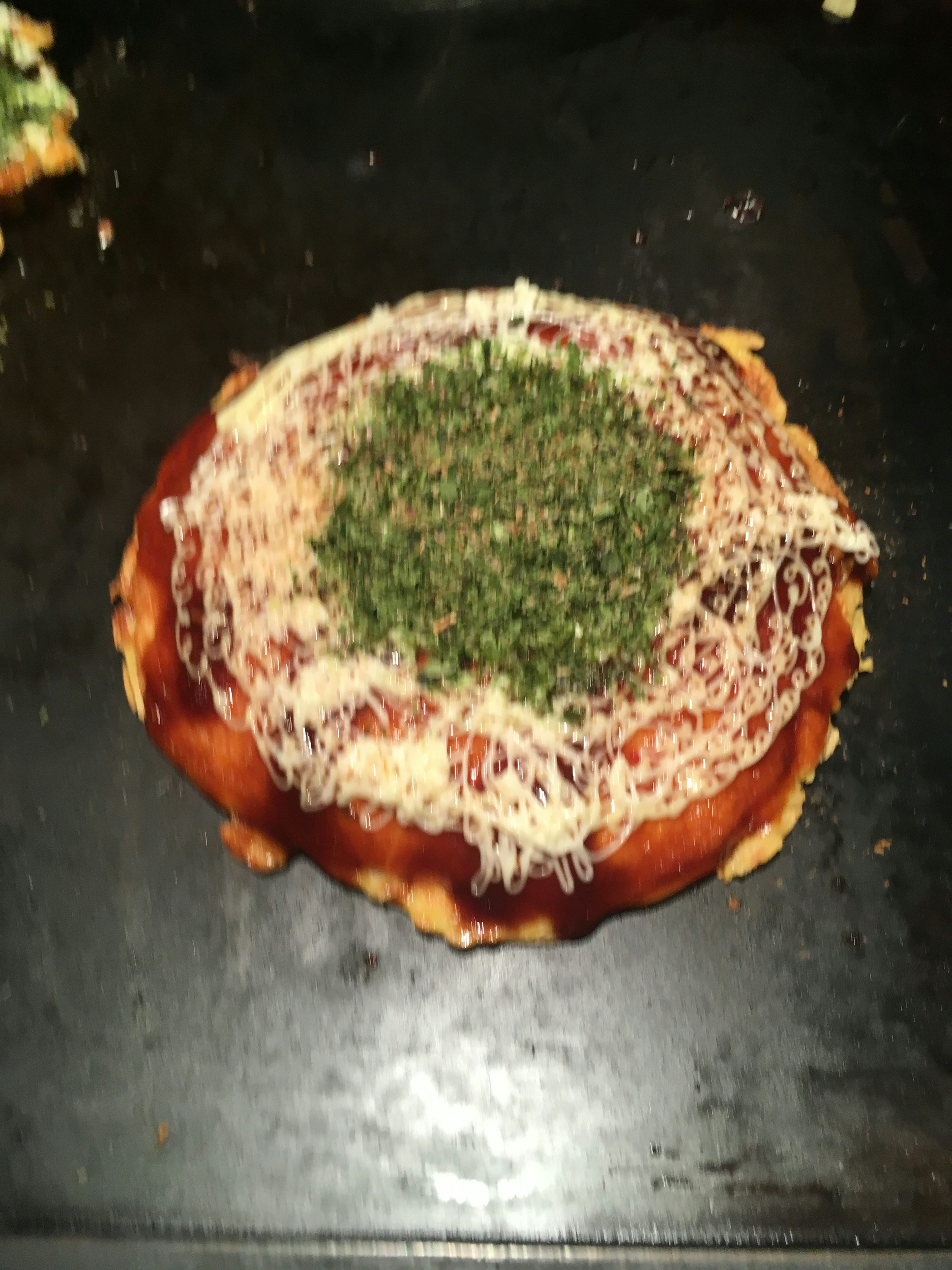 Pizza garnie de fromage et d'herbes sur une plaque de cuisson sombre