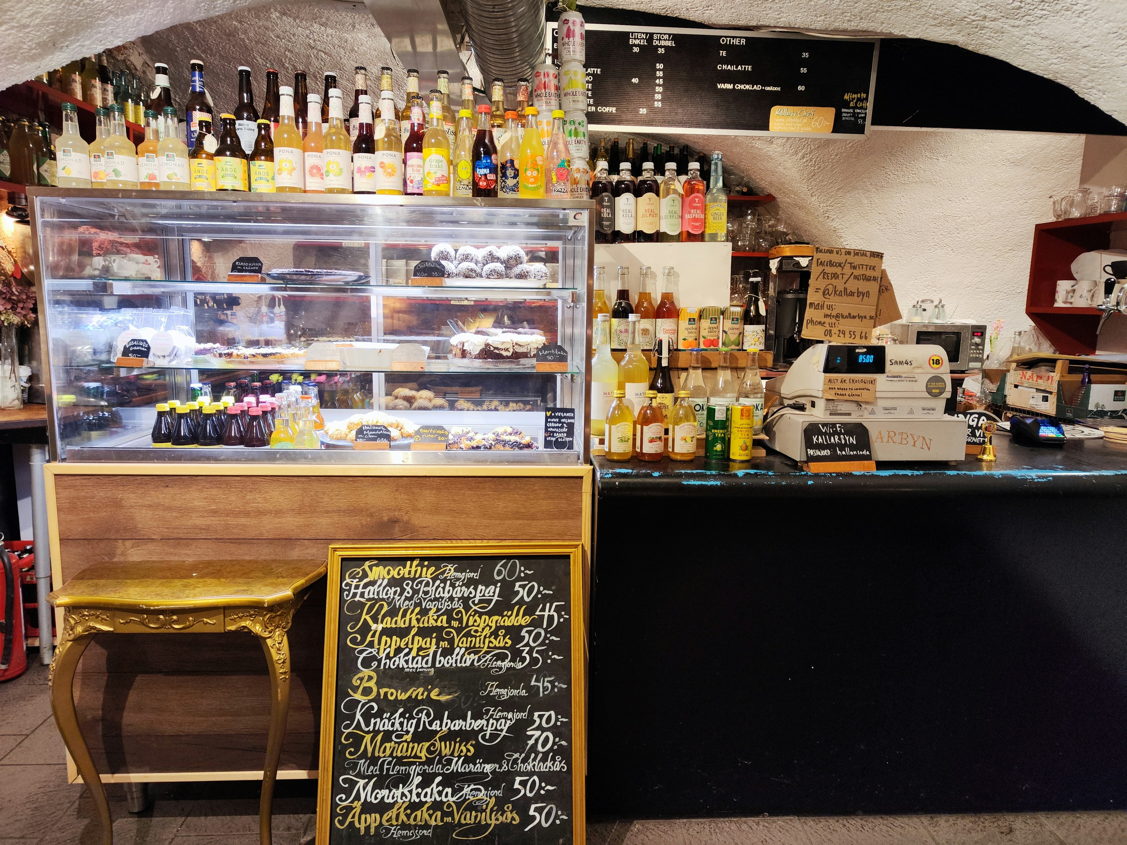 Vista interior de una cafetería con una vitrina de postres y un mostrador de bebidas