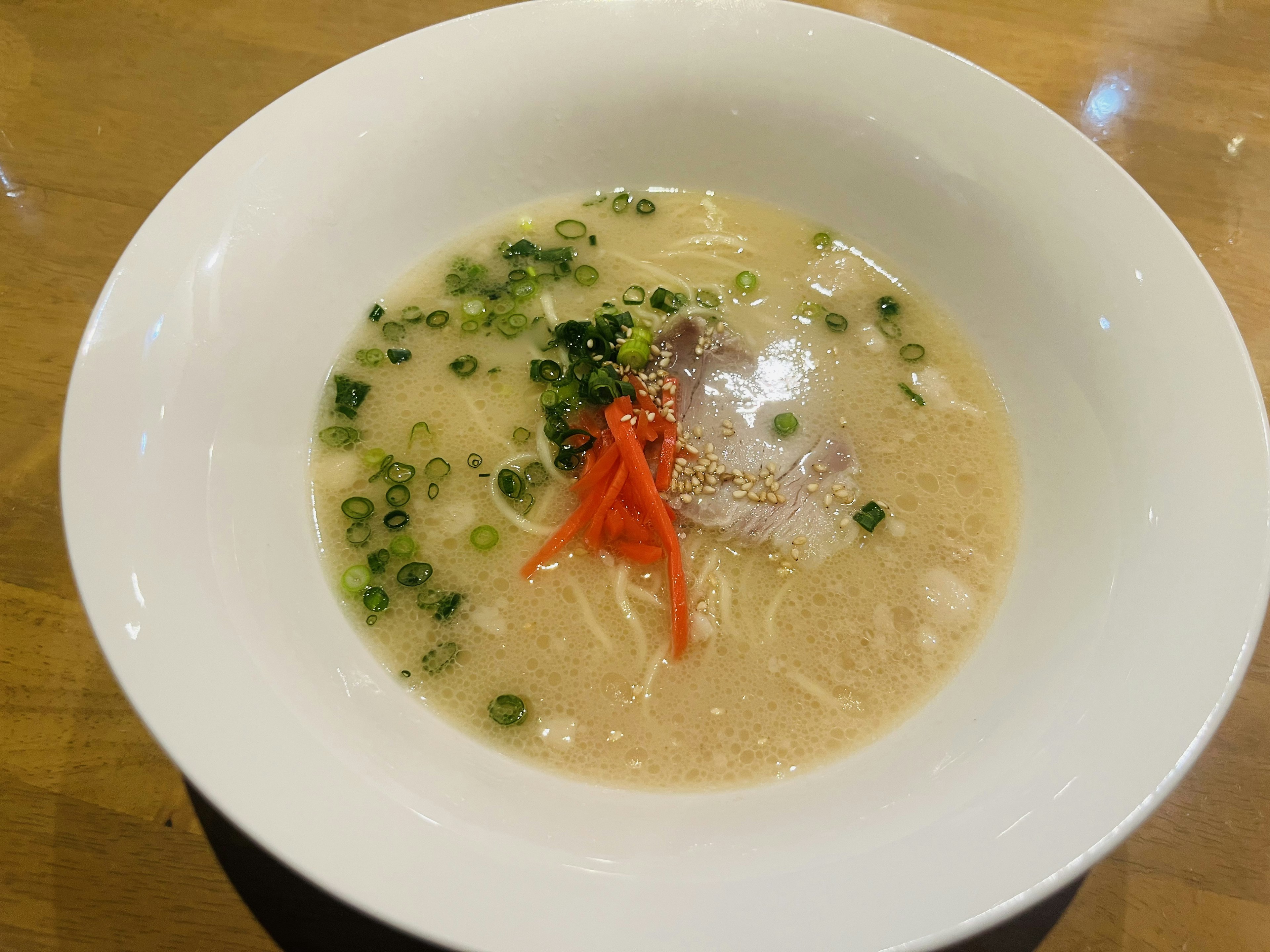 Zuppa di ramen in una ciotola bianca guarnita con cipolle verdi e zenzero marinato