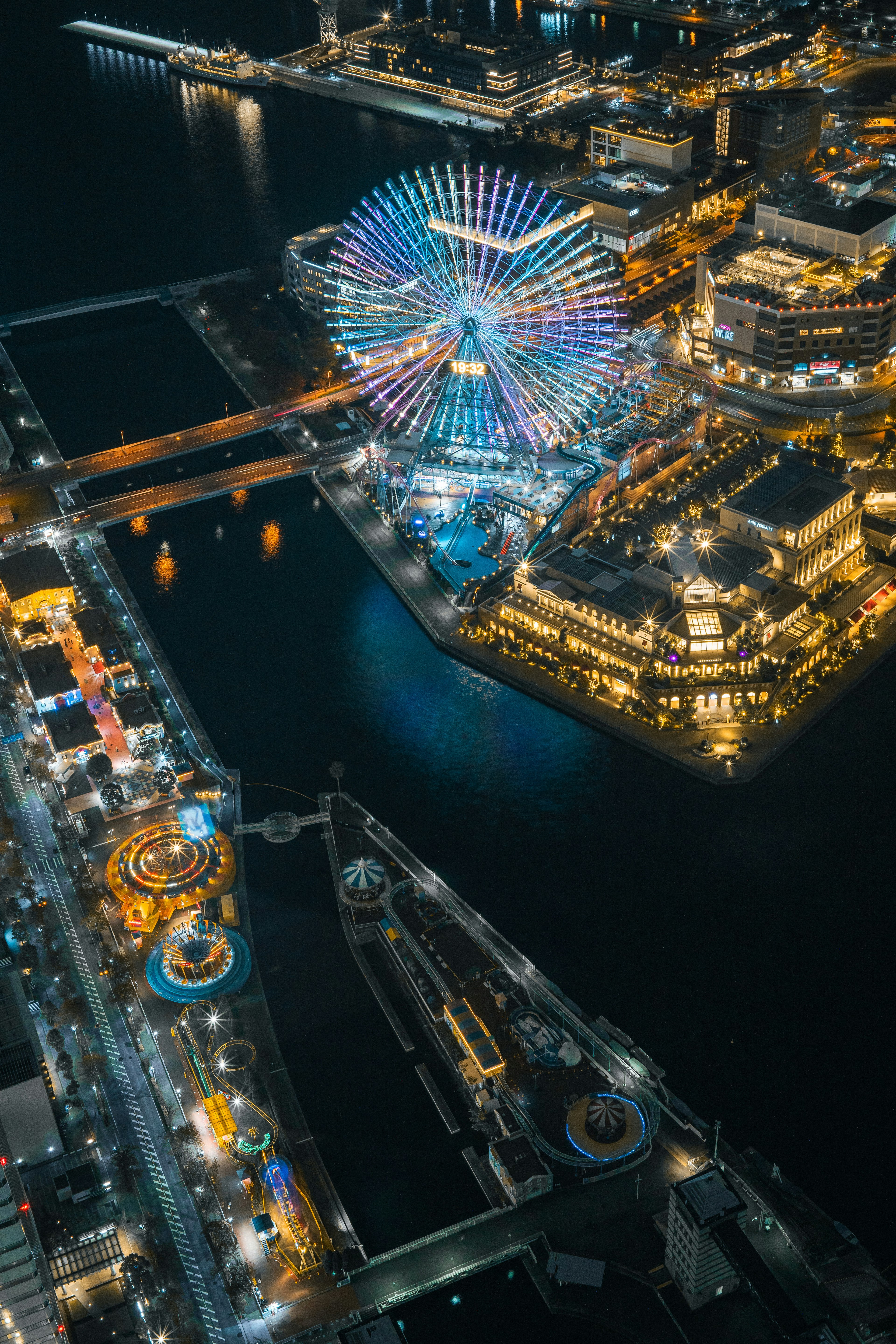 Aerial view of a colorful Ferris wheel and amusement park by the waterfront at night