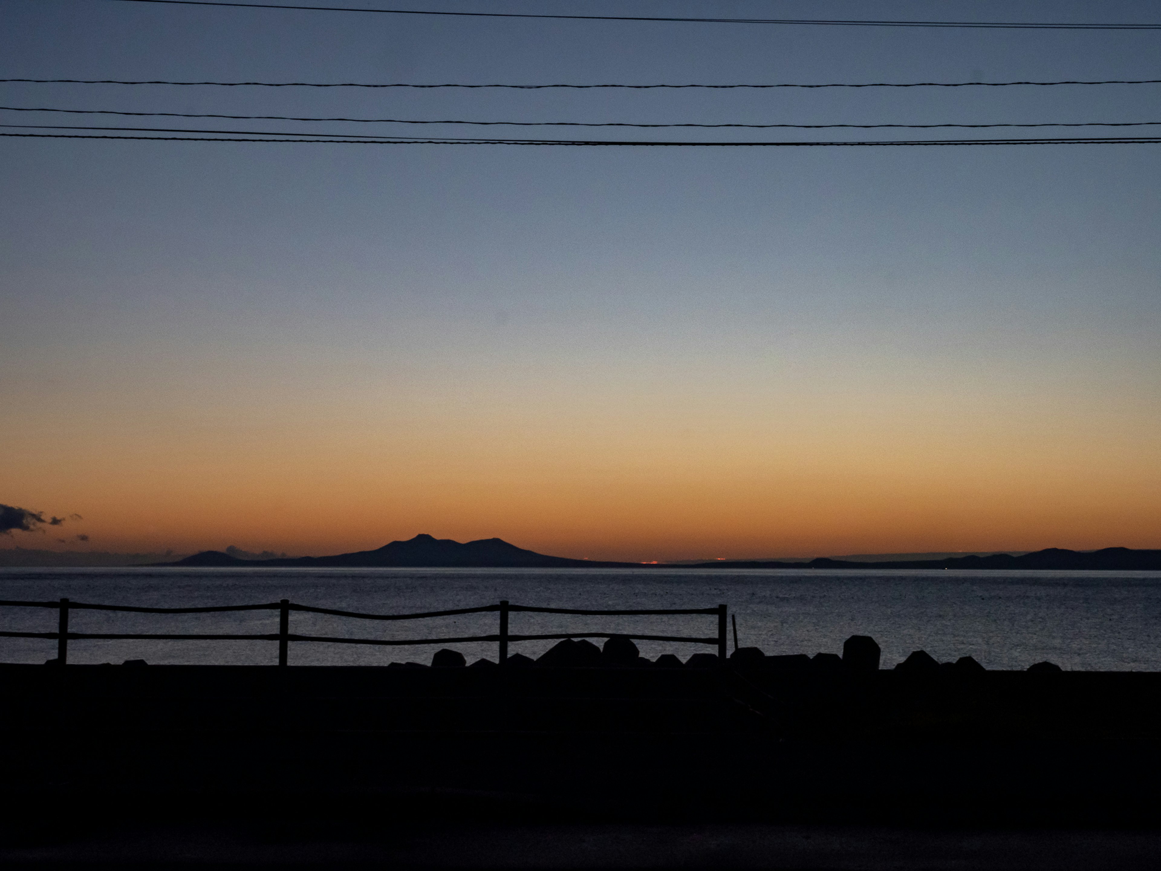 Silhouette of mountains against a sunset over the sea