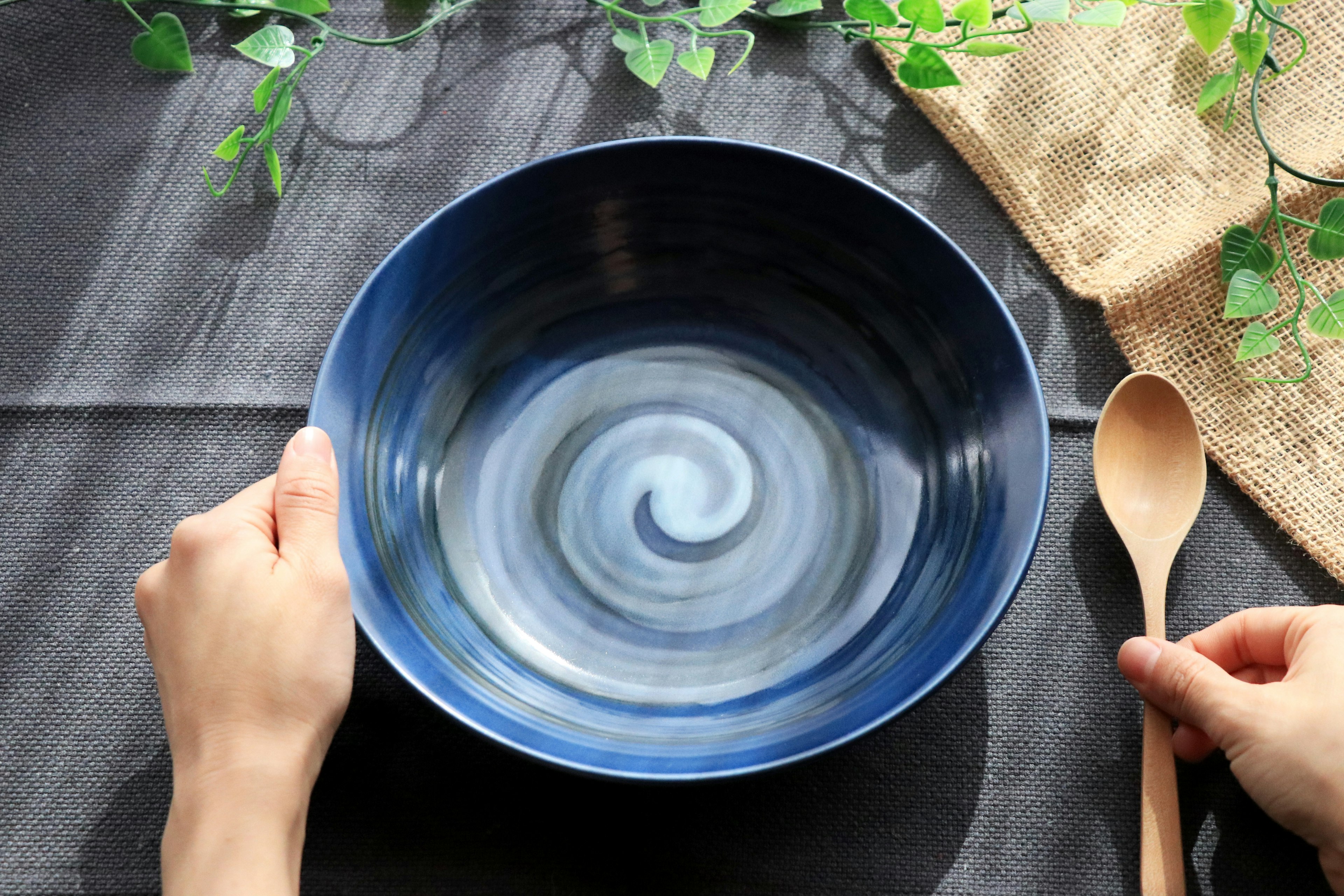 Hands holding a blue swirling bowl with a wooden spoon on a textured table