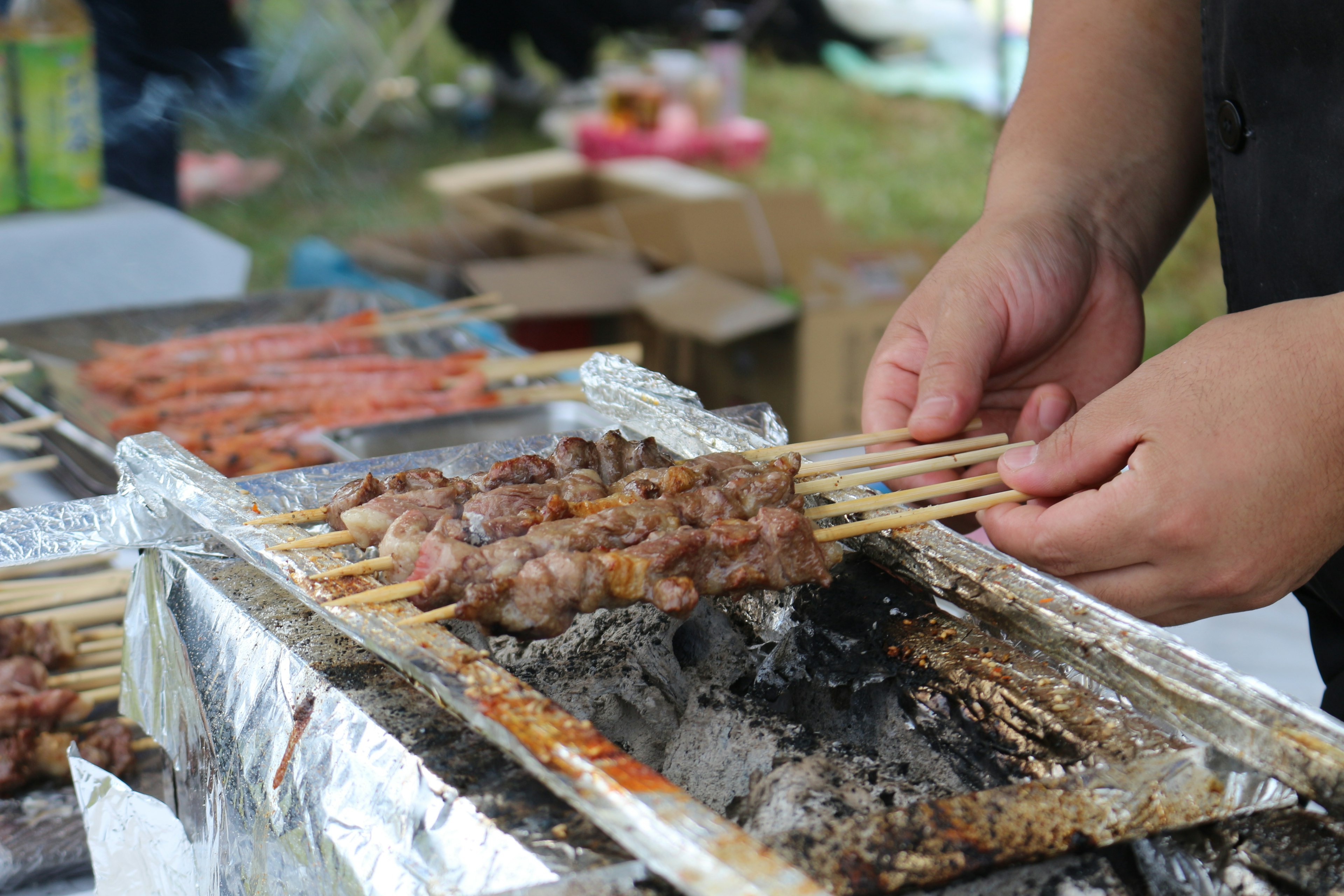 肉串を焼いている手のアップ画像 バーベキューグリルの上で焼かれた肉串