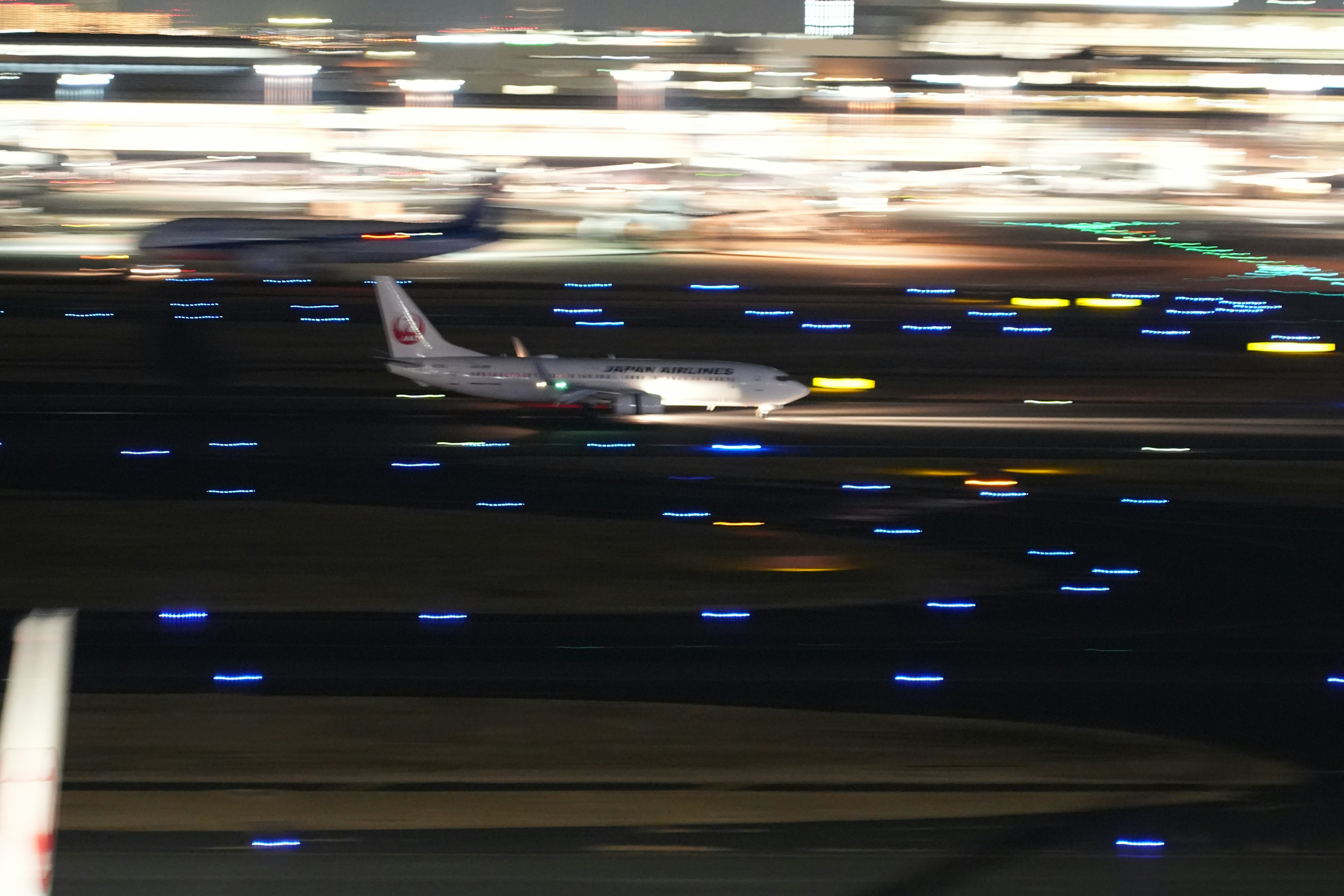 An airplane taxiing on a runway at night with blurred motion and colorful lights