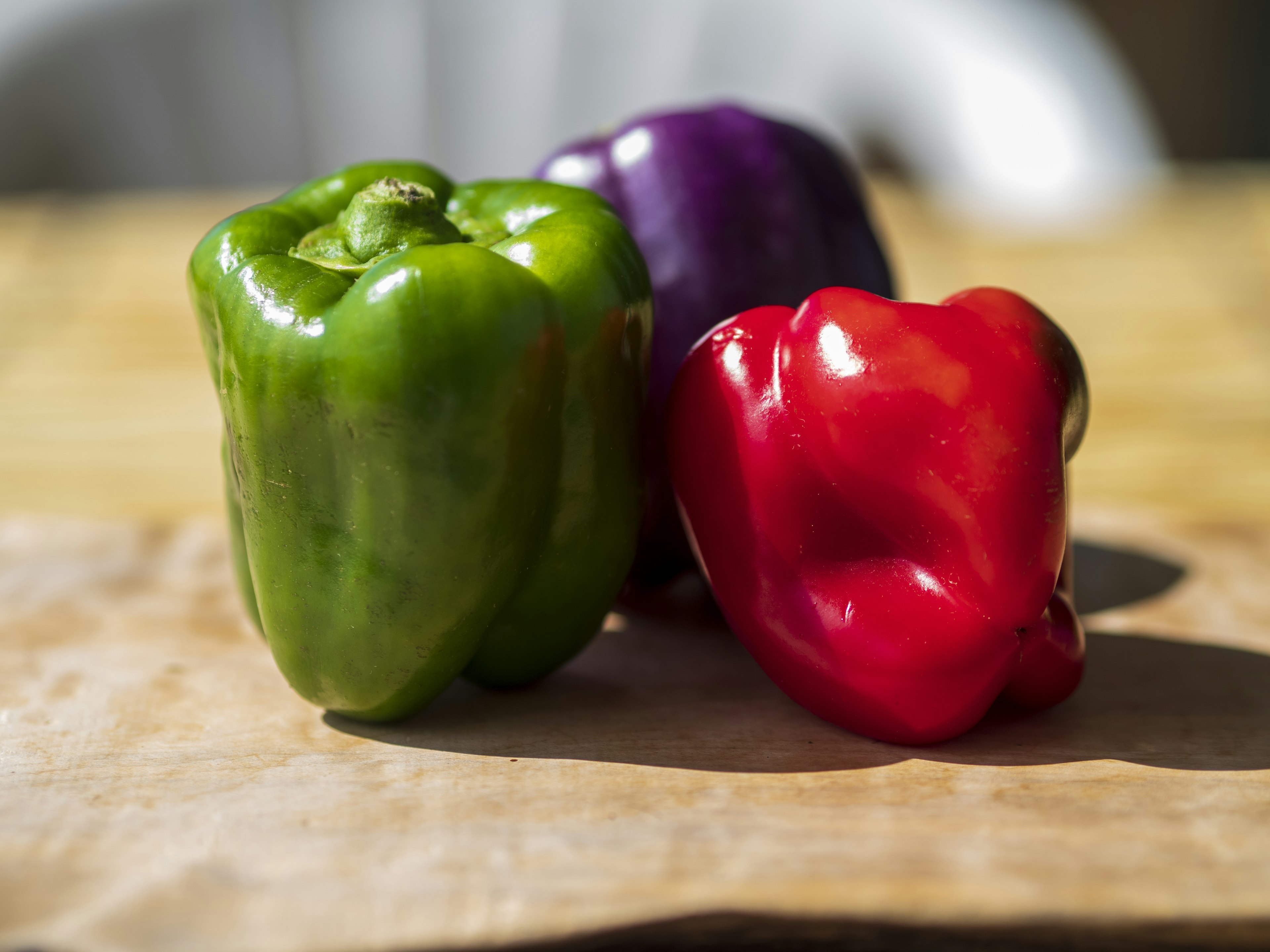 Green red and purple bell peppers arranged on a wooden cutting board