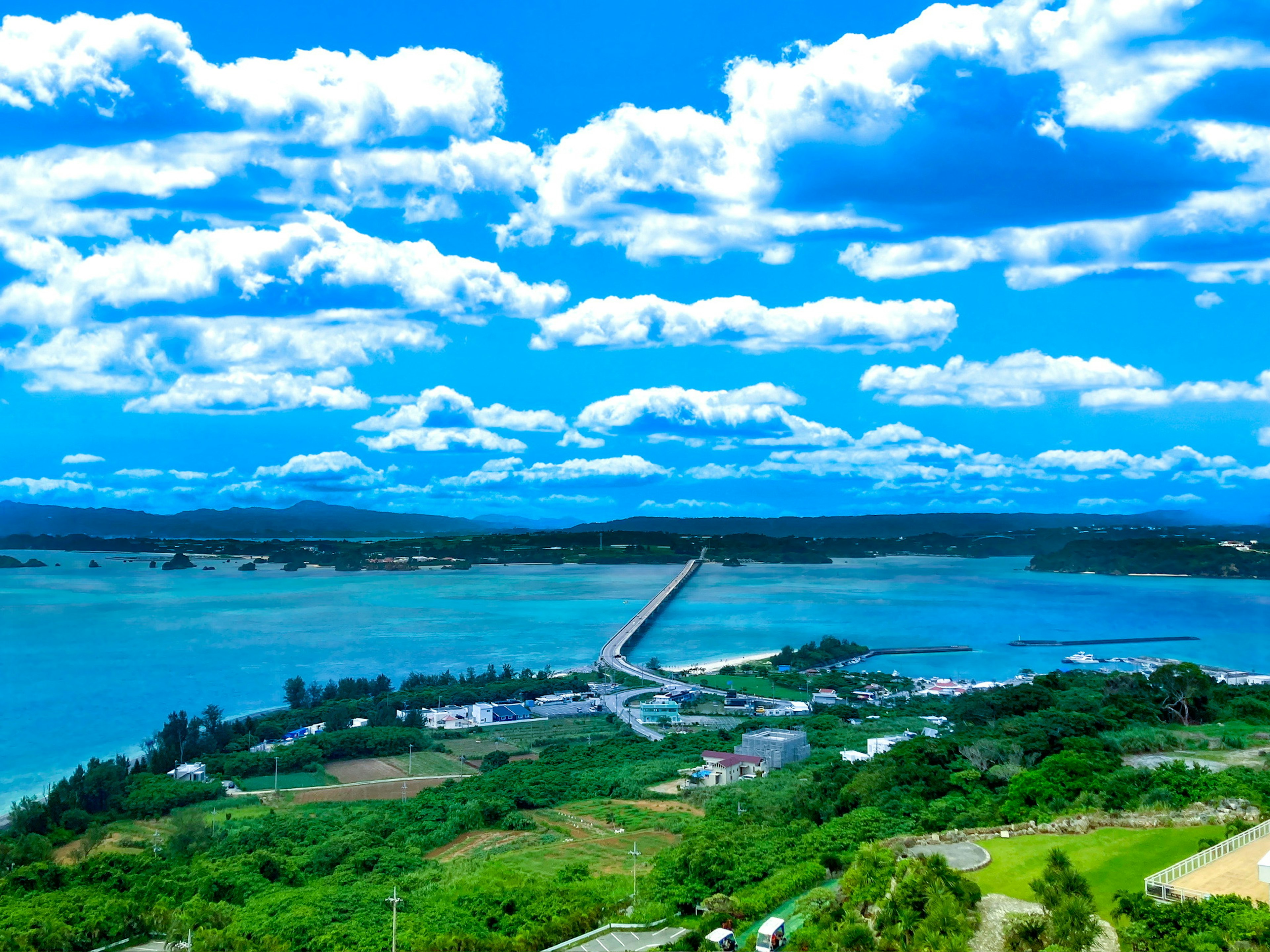 Vista panoramica del mare blu e del cielo con nuvole bianche terra verde lussureggiante e un ponte