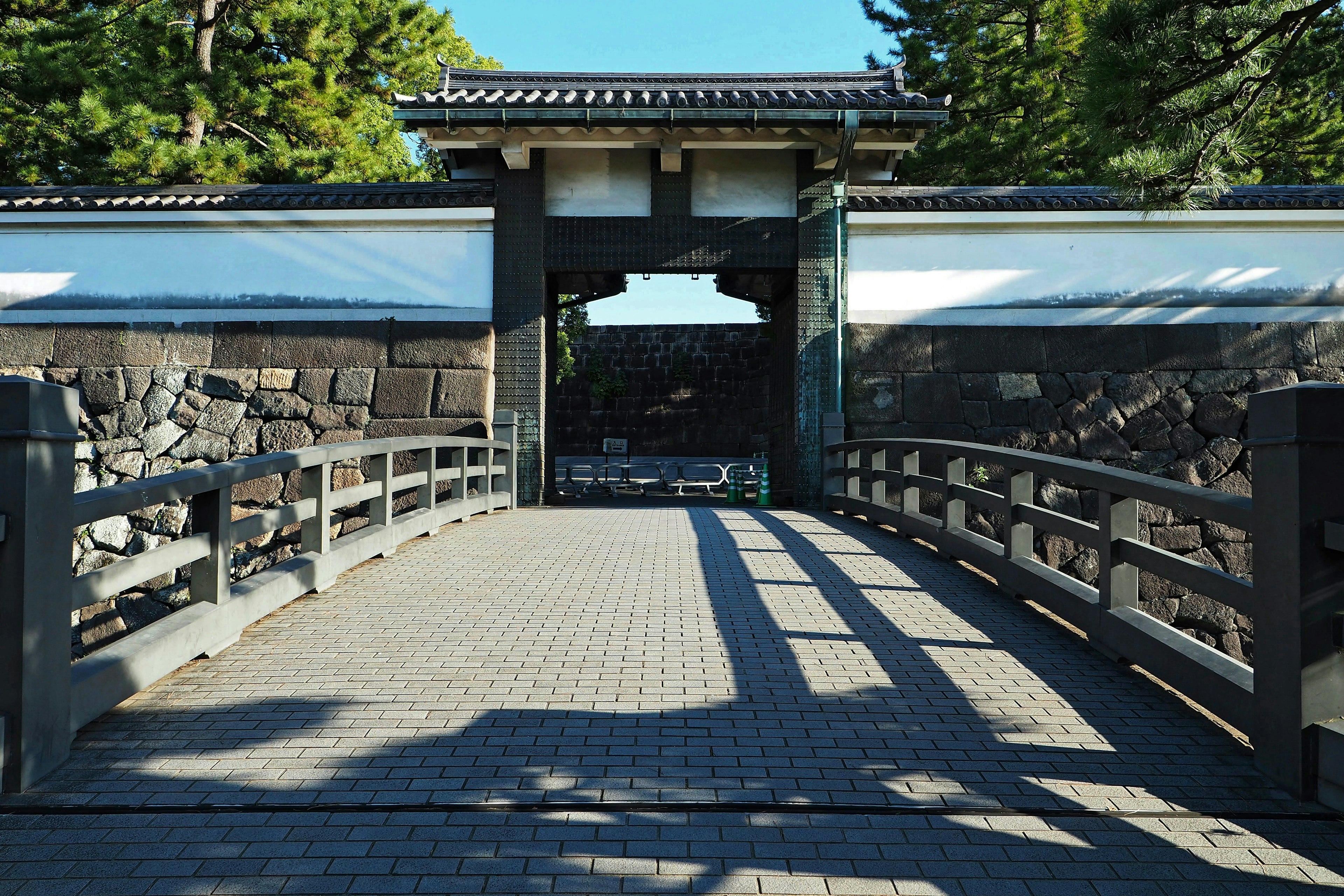 Escena de puerta y puente japonés tradicional con muros de piedra y árboles visibles