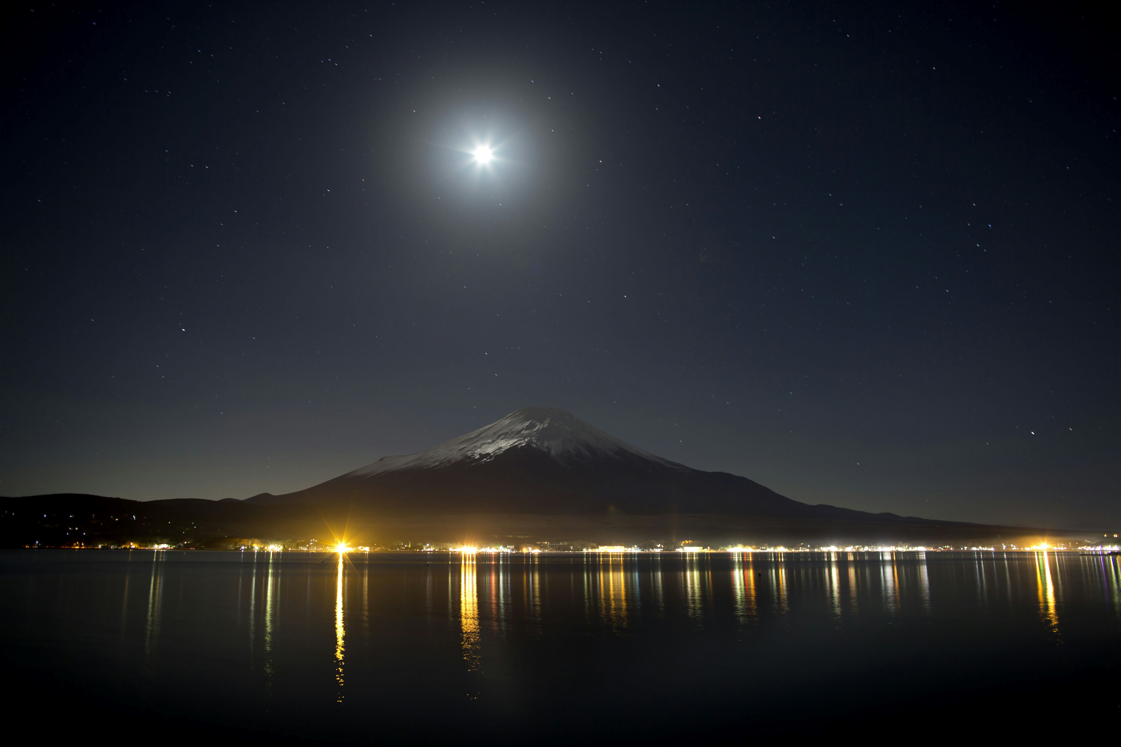 Un paysage nocturne serein avec une lune brillante et son reflet sur un lac calme