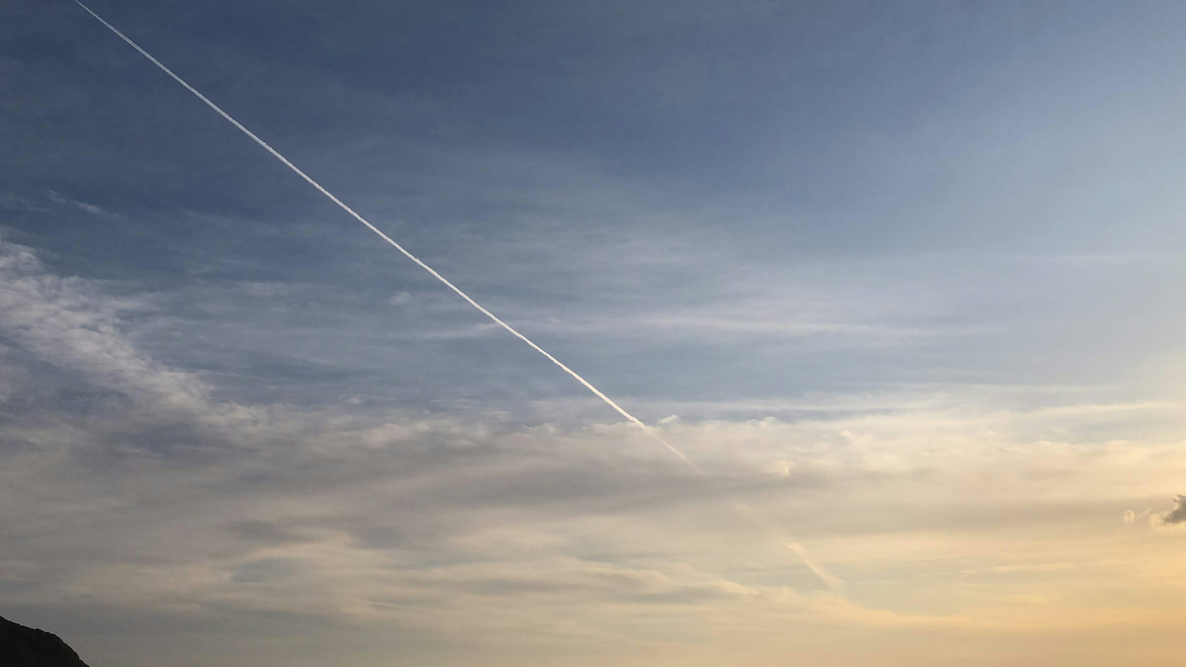 空に飛行機雲が見える青い空と夕焼けの雲