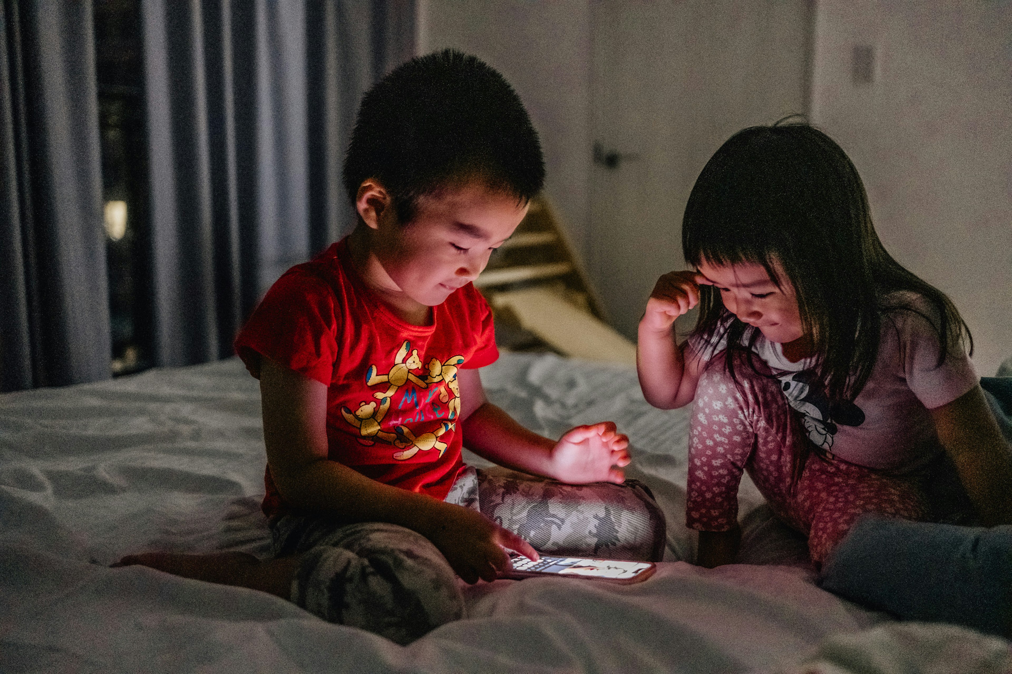 Kinder konzentrieren sich auf ein Smartphone, während sie auf einem Bett sitzen