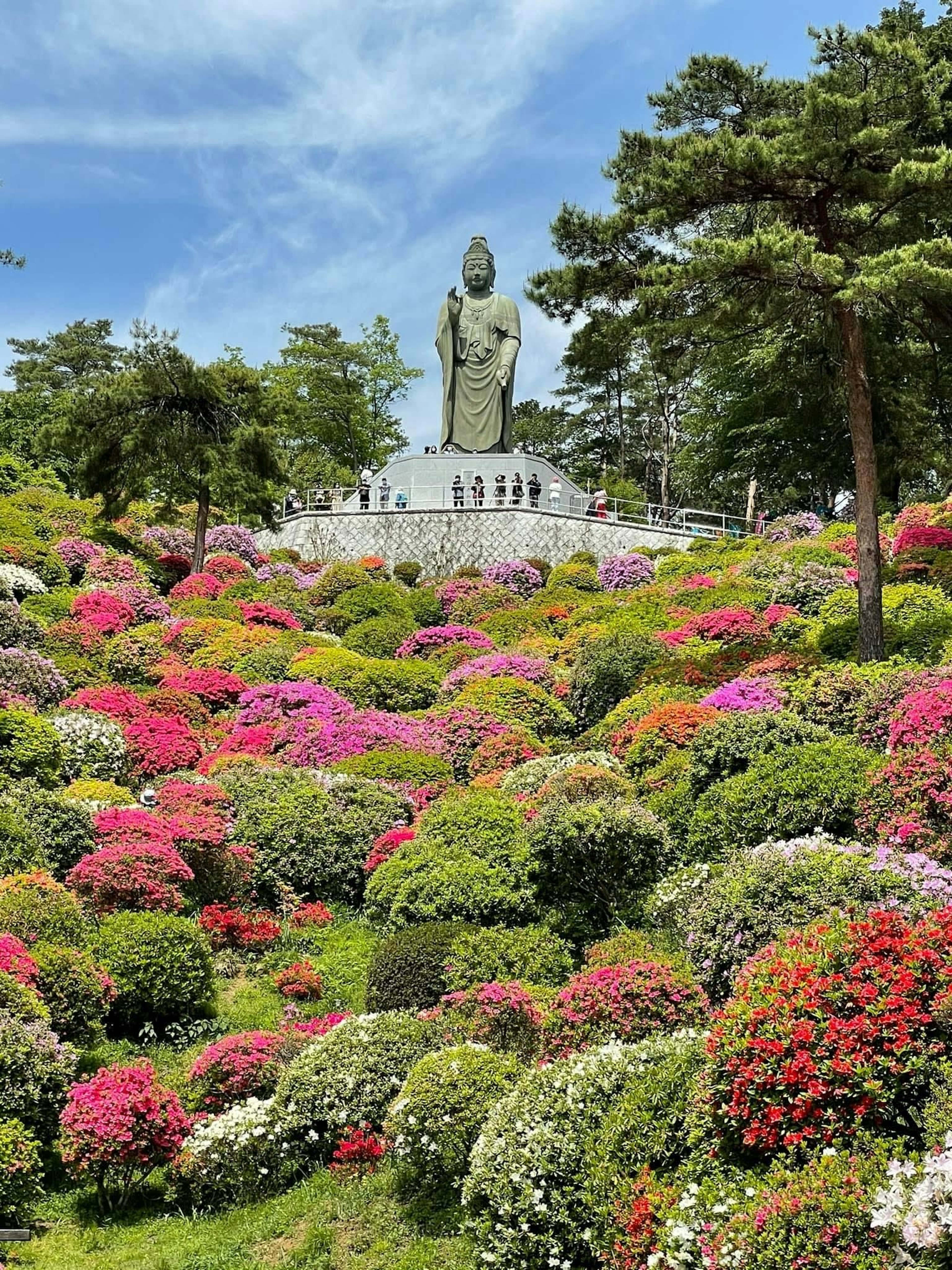 色とりどりの花に囲まれた大きな仏像の彫刻が見える美しい庭