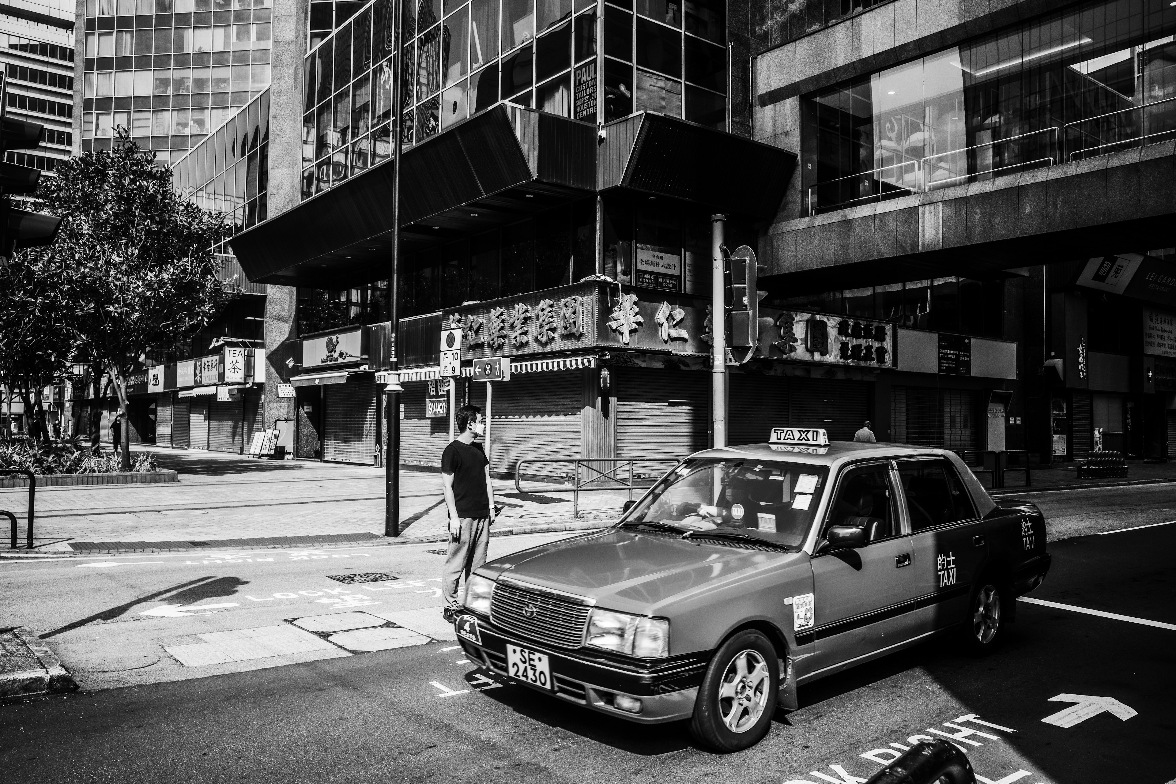 A black and white urban scene featuring a parked taxi and a pedestrian