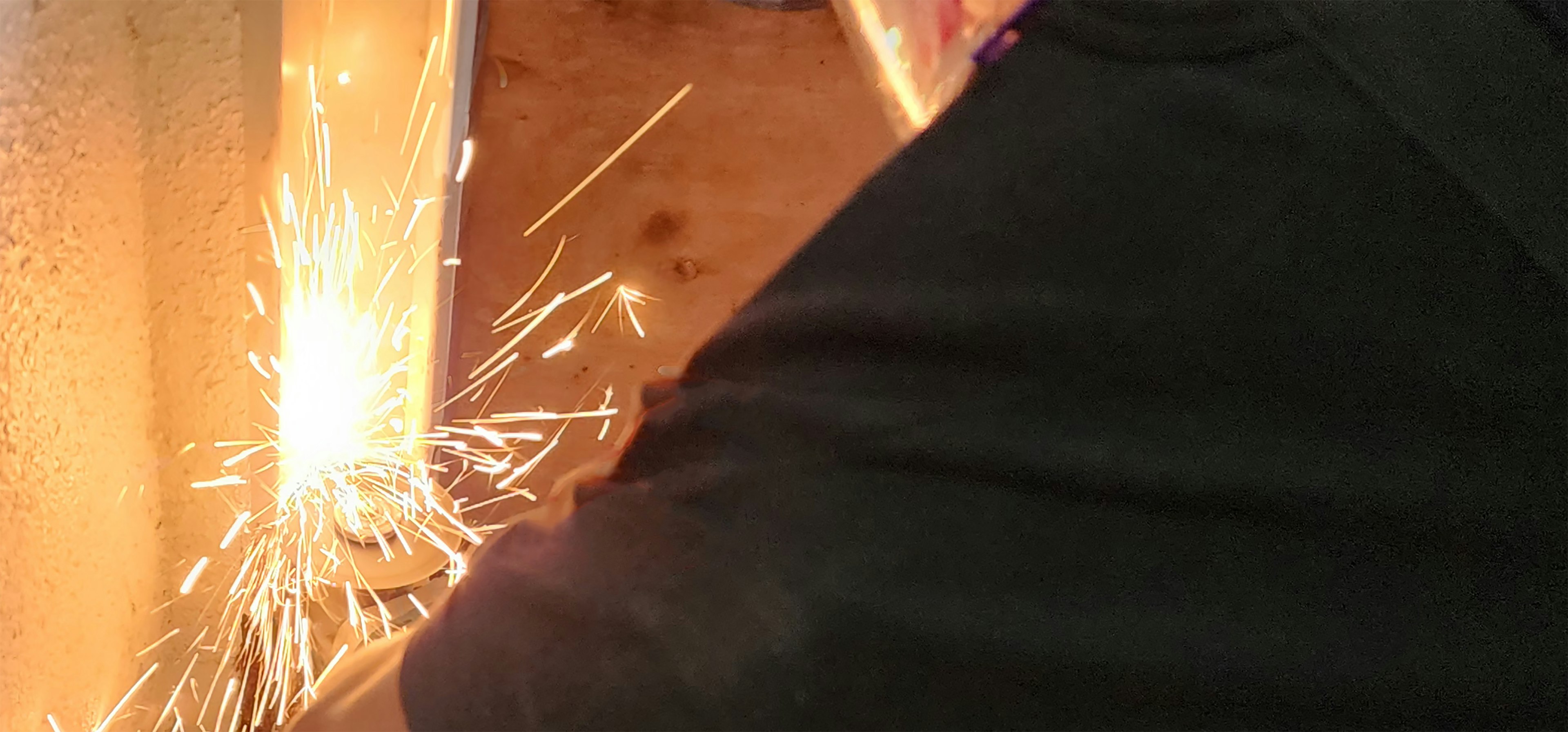 A worker's hand processing metal while sparks fly