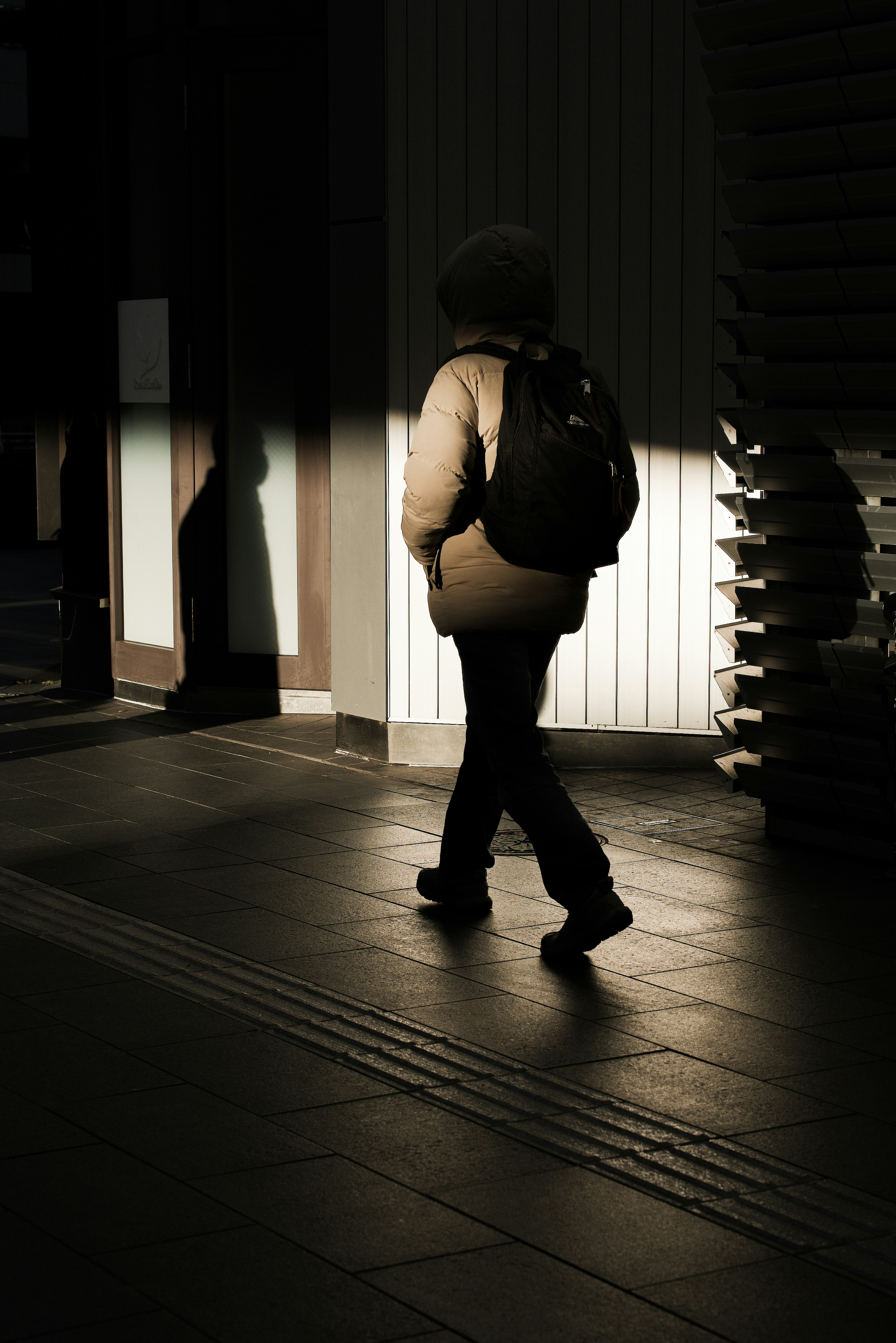 Silhouette of a person walking with a backpack in a partially lit urban setting