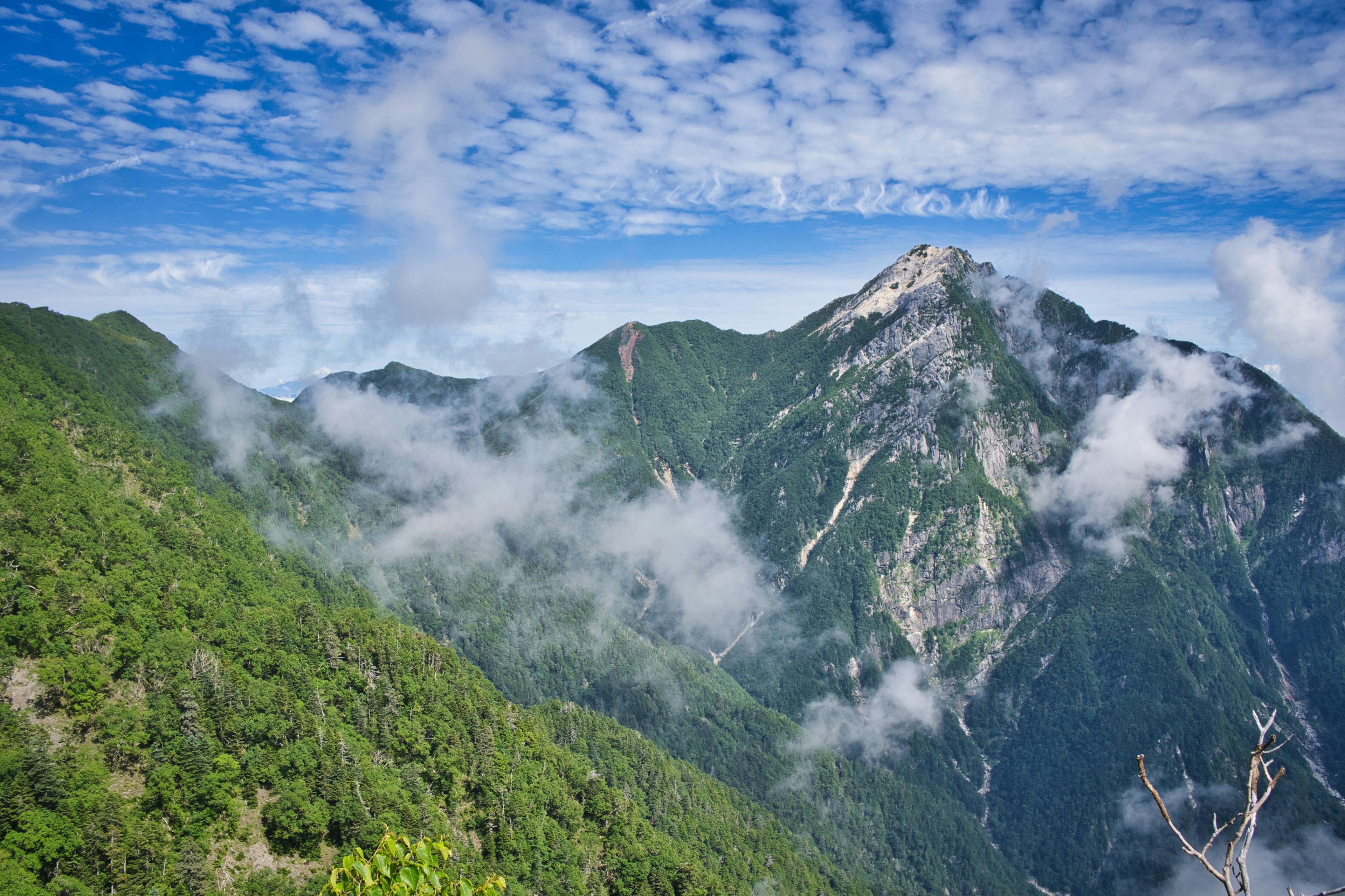 青い空と白い雲に囲まれた緑の山々の風景