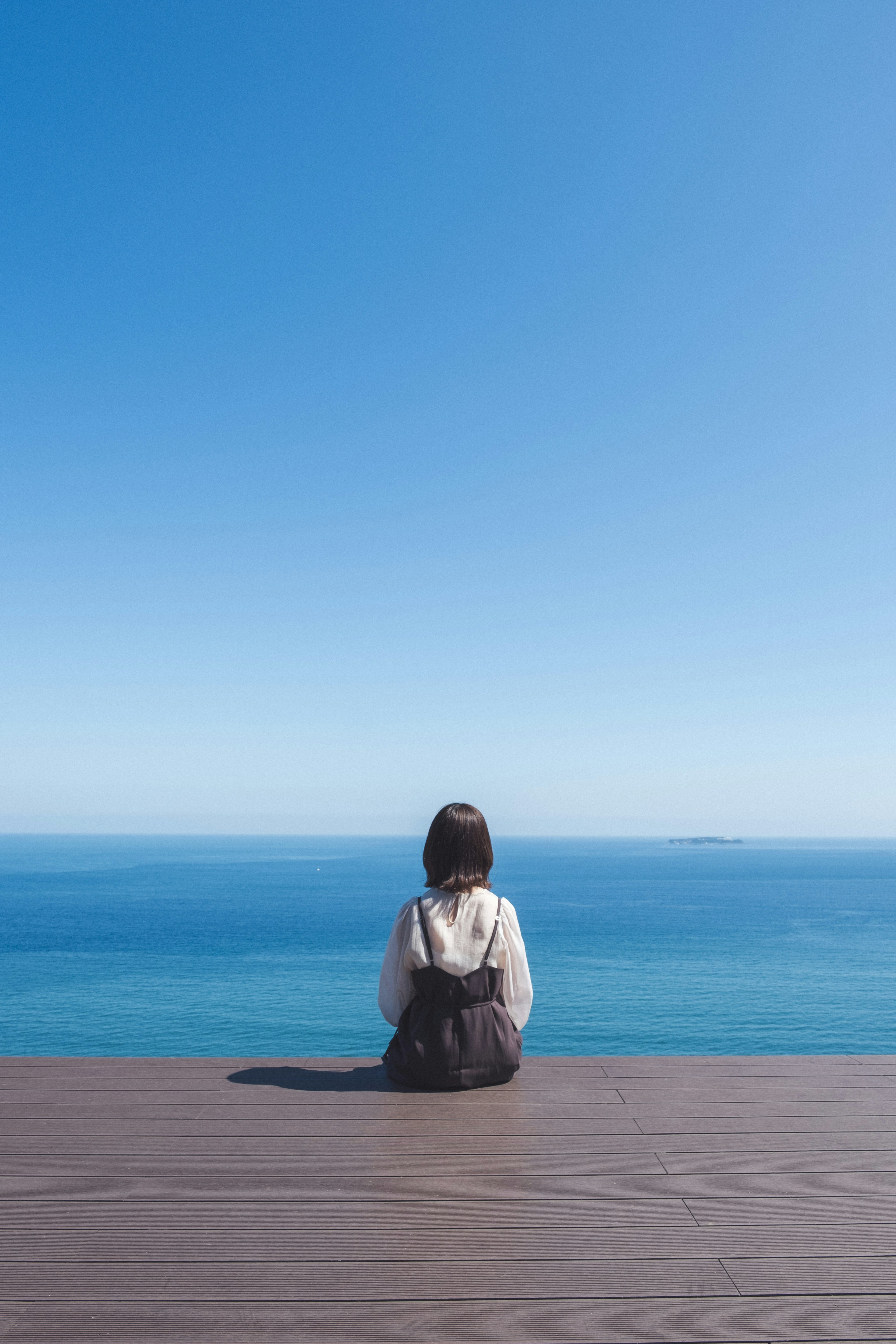 A woman sitting on a deck looking at the blue ocean