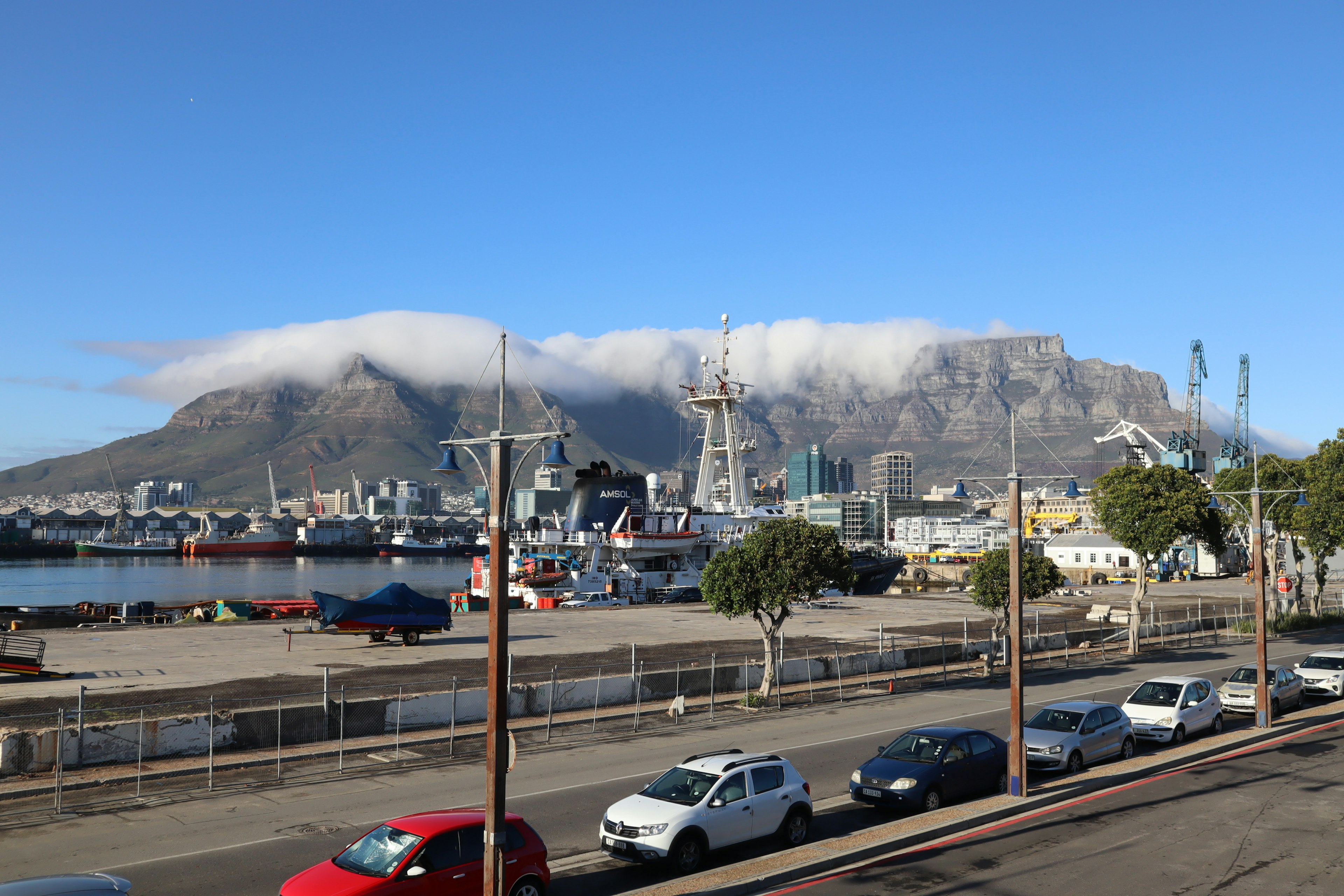 Aussicht auf den Tafelberg mit Wolken Hafenansicht mit Booten und geparkten Autos