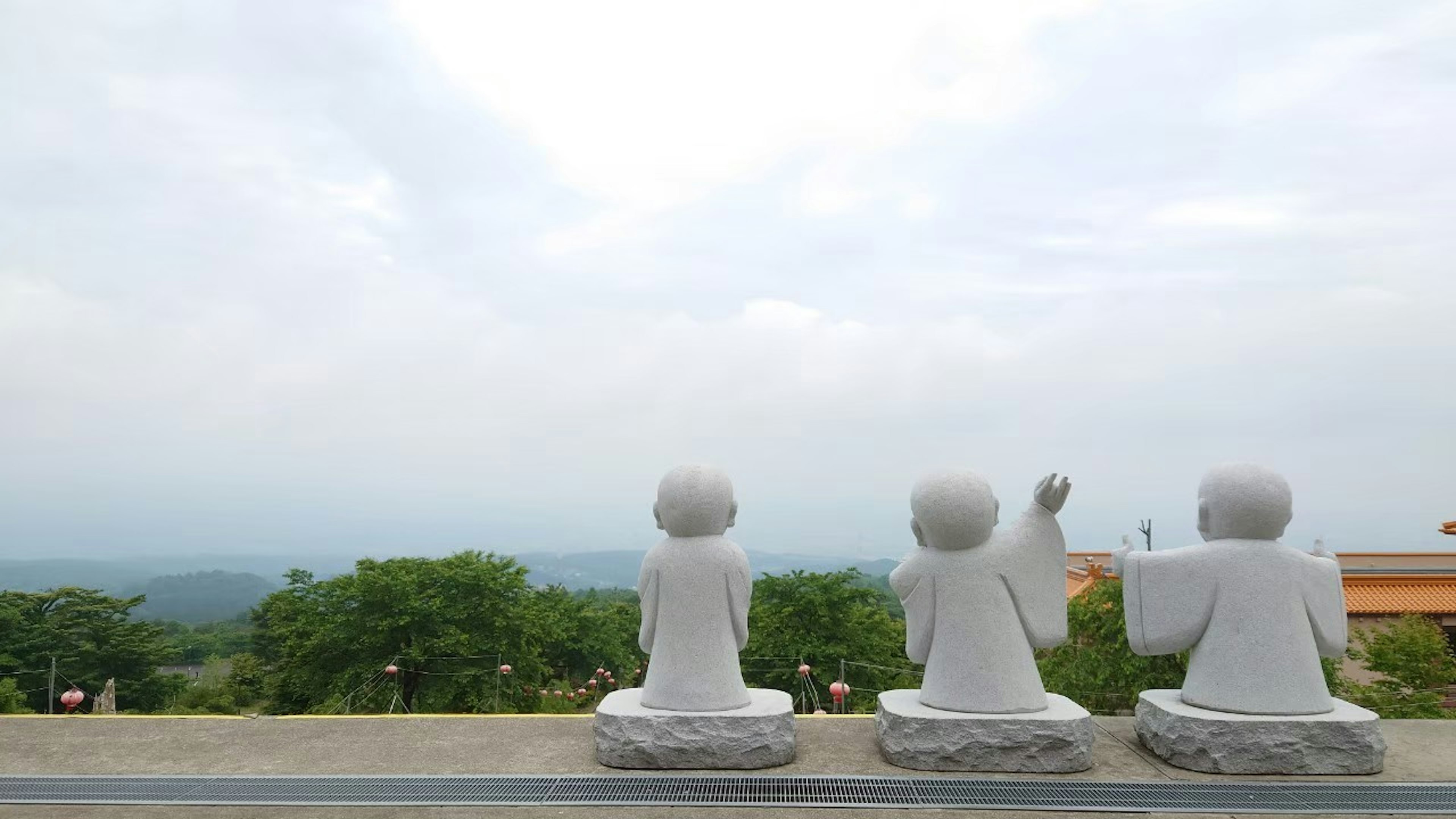 Three white Buddha statues seated with a scenic view of green trees and cloudy sky