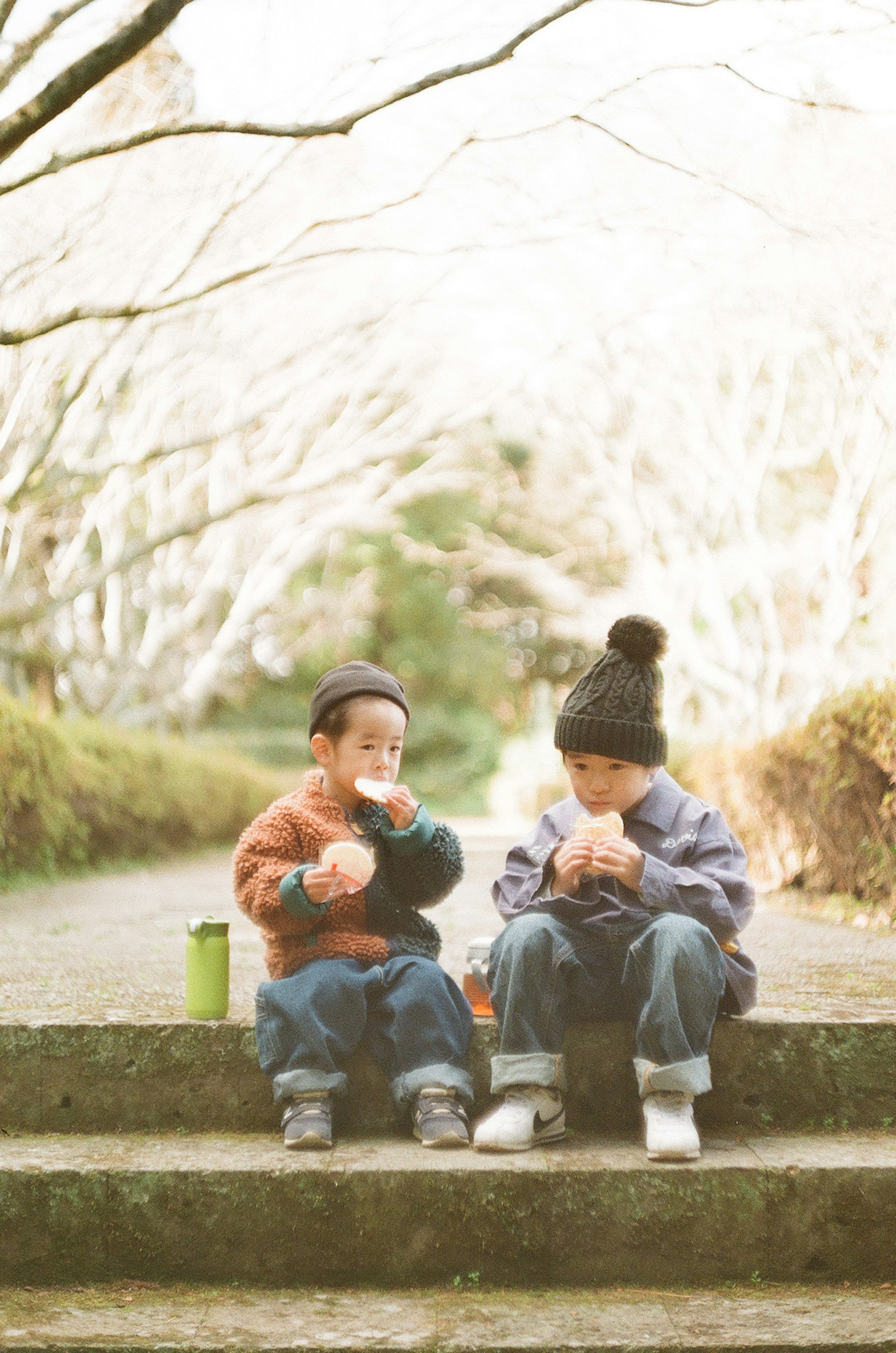 Two children sitting on steps in a park enjoying snacks