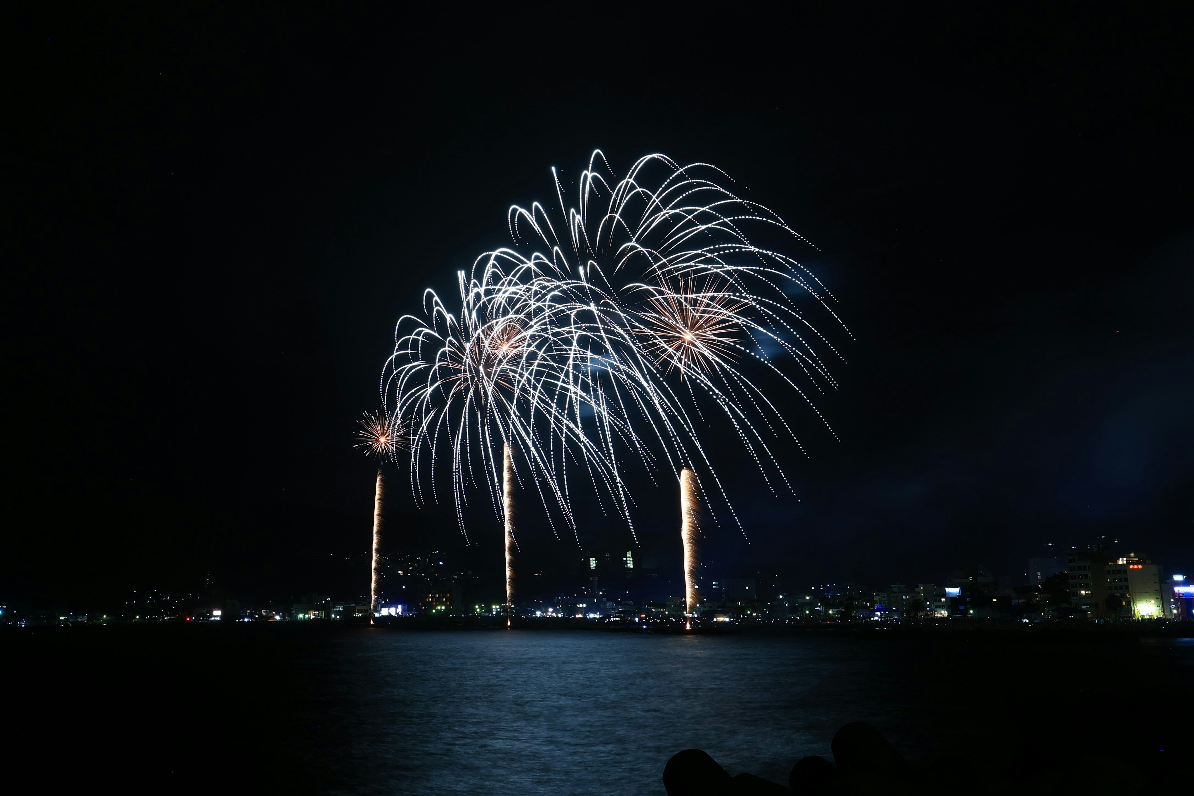 Hermoso espectáculo de fuegos artificiales reflejándose en el agua por la noche