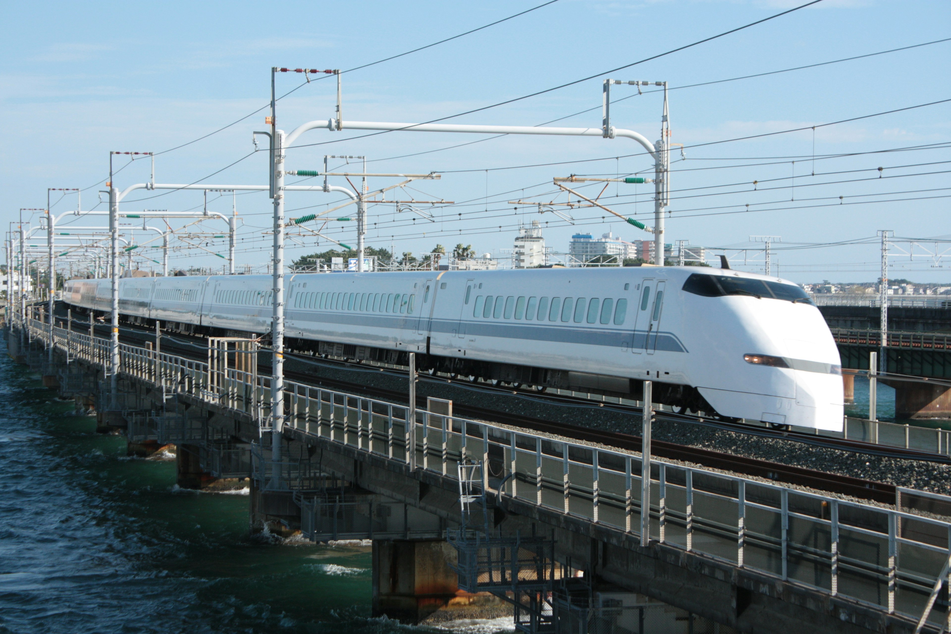 Shinkansen melintasi jembatan dengan langit biru dan air di bawah