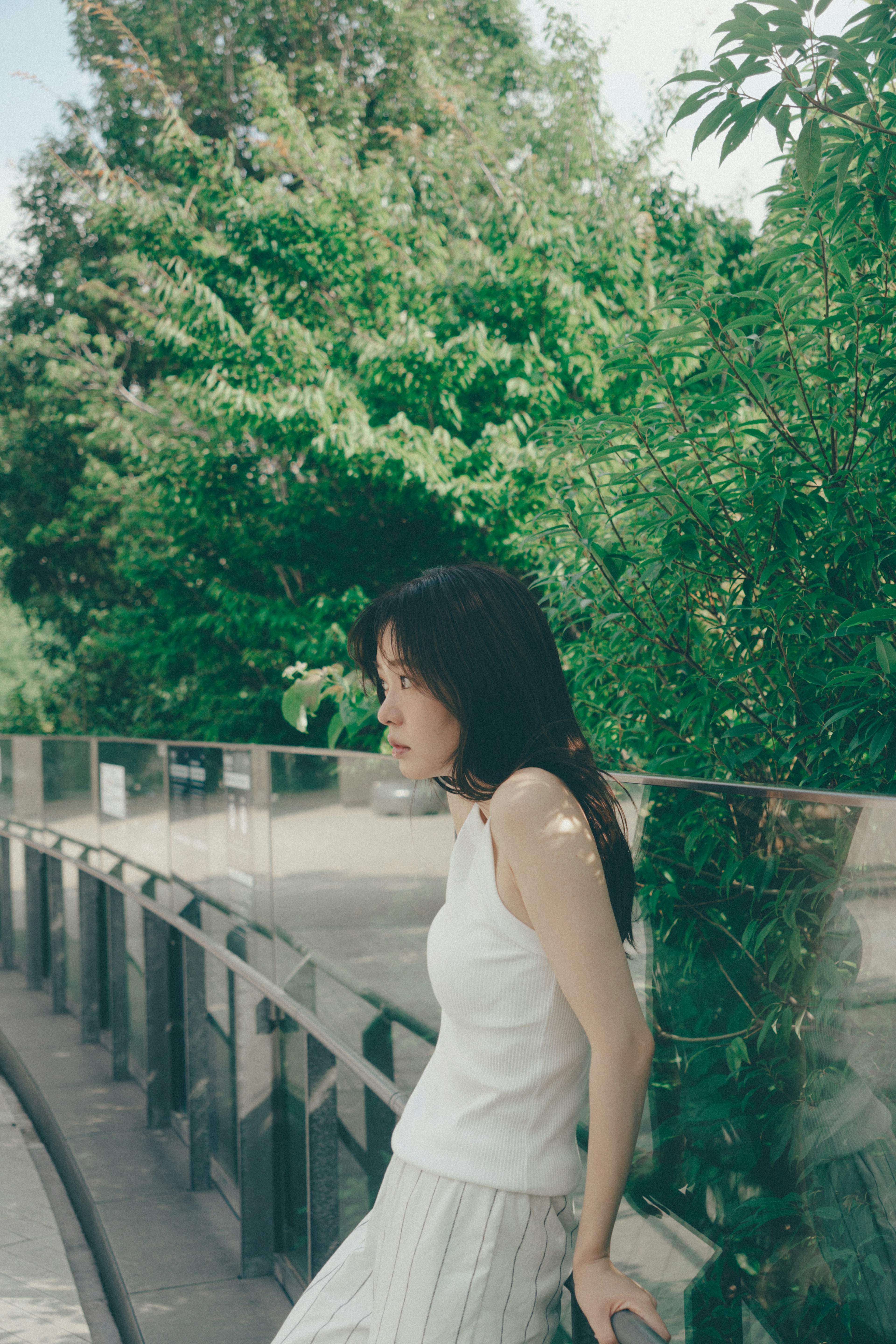 Side profile of a woman in a white top surrounded by lush greenery