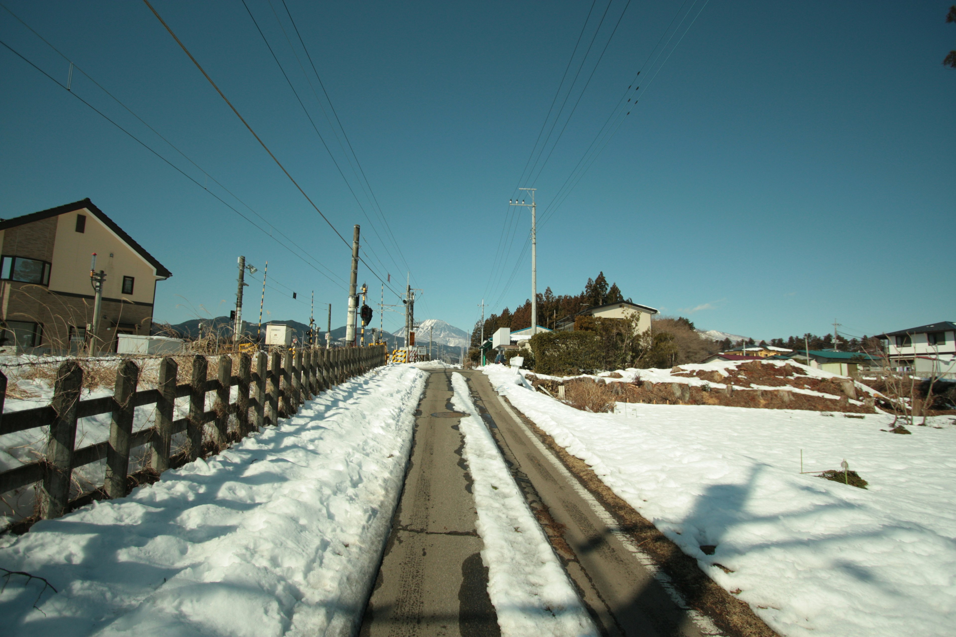 Camino cubierto de nieve con casas circundantes bajo un cielo azul