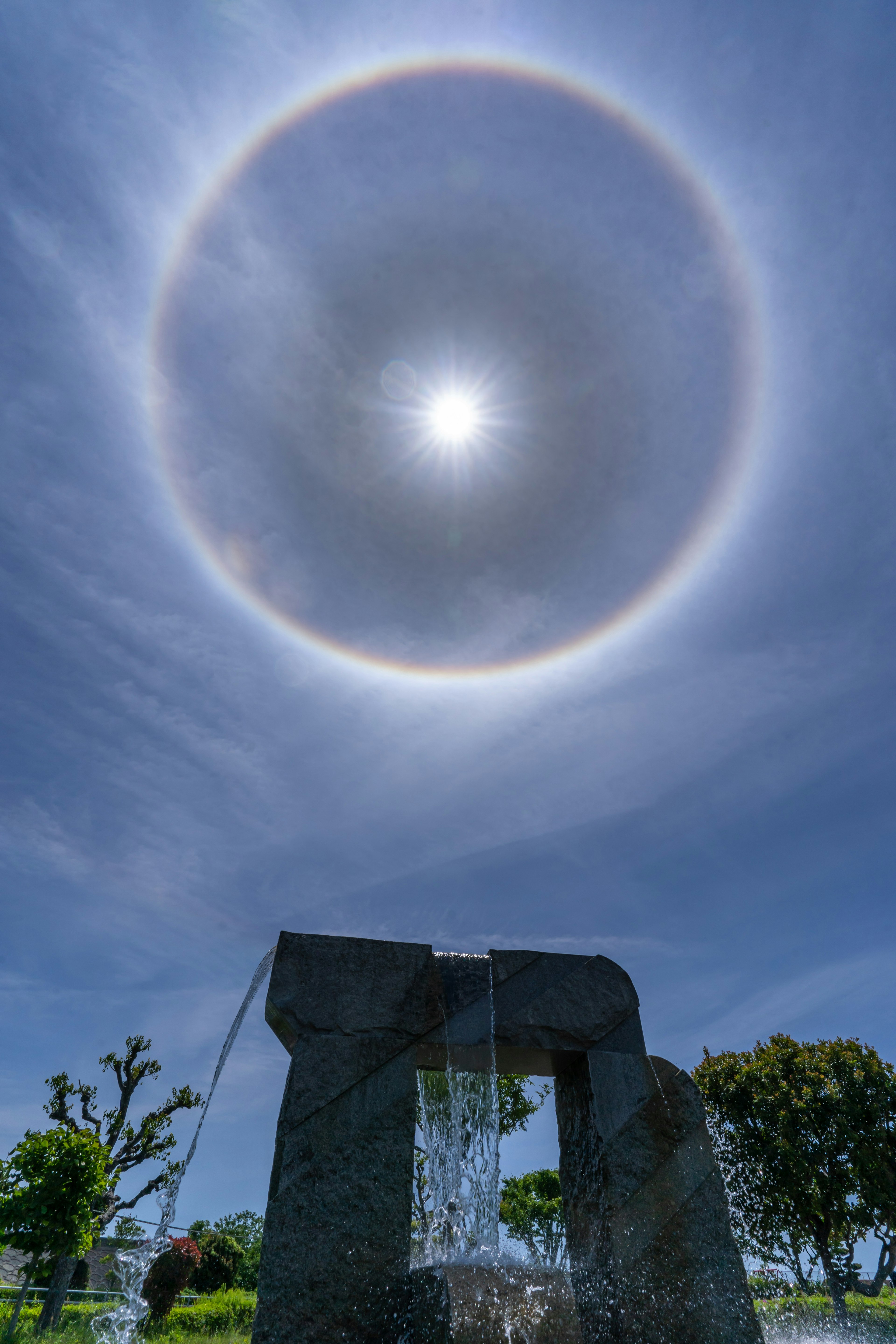 Scultura in pietra sotto un cielo blu con un alone attorno al sole