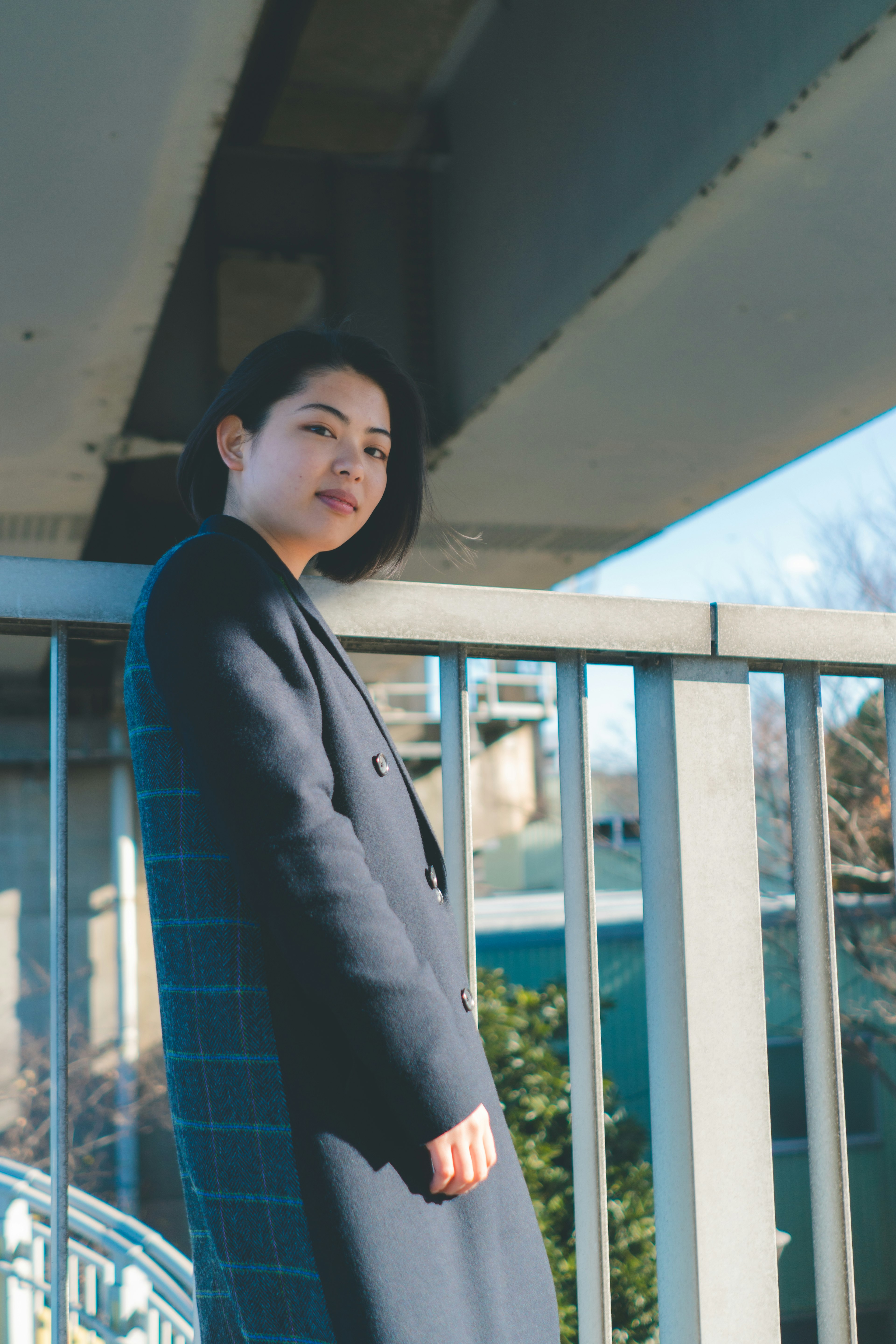 Portrait of a woman leaning against a bridge under a blue sky