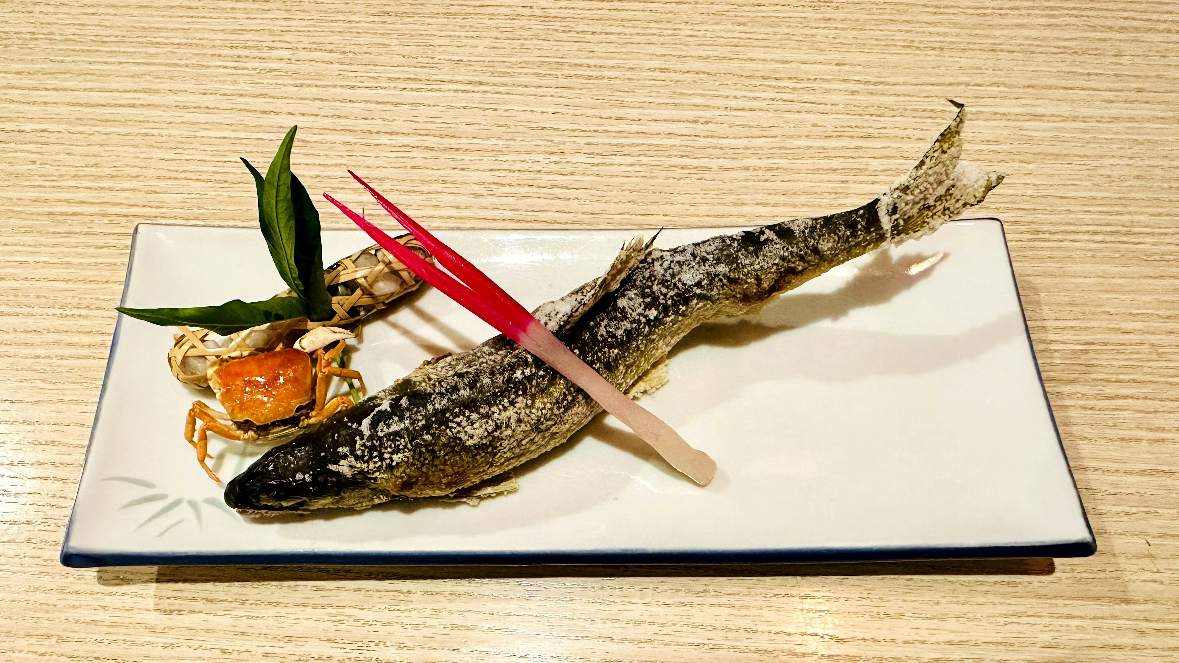 Pescado a la parrilla en un plato con un pequeño aperitivo y hojas decorativas