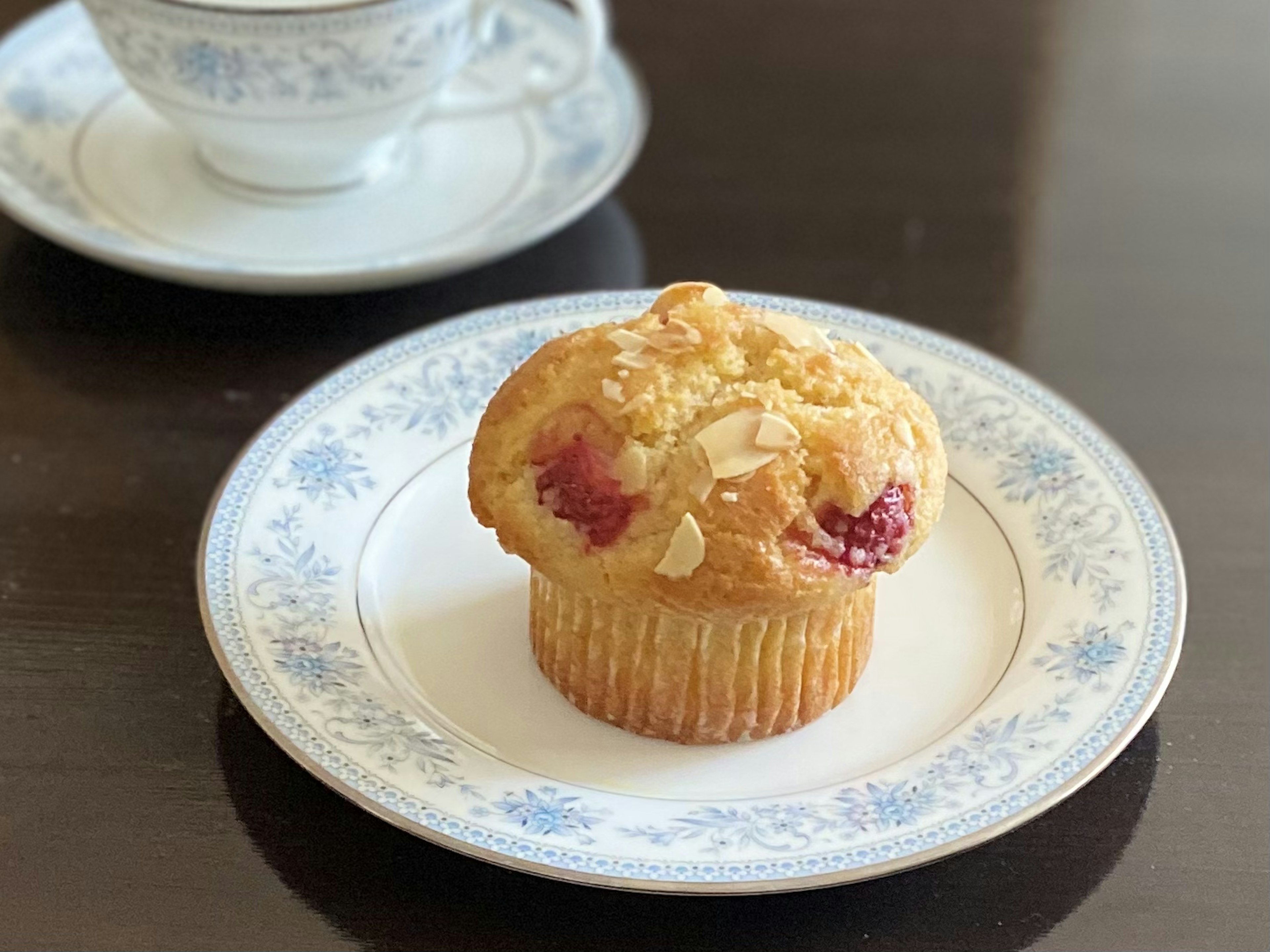 Himbeer-Mandel-Muffin auf einem dekorativen Teller mit einer Teetasse im Hintergrund