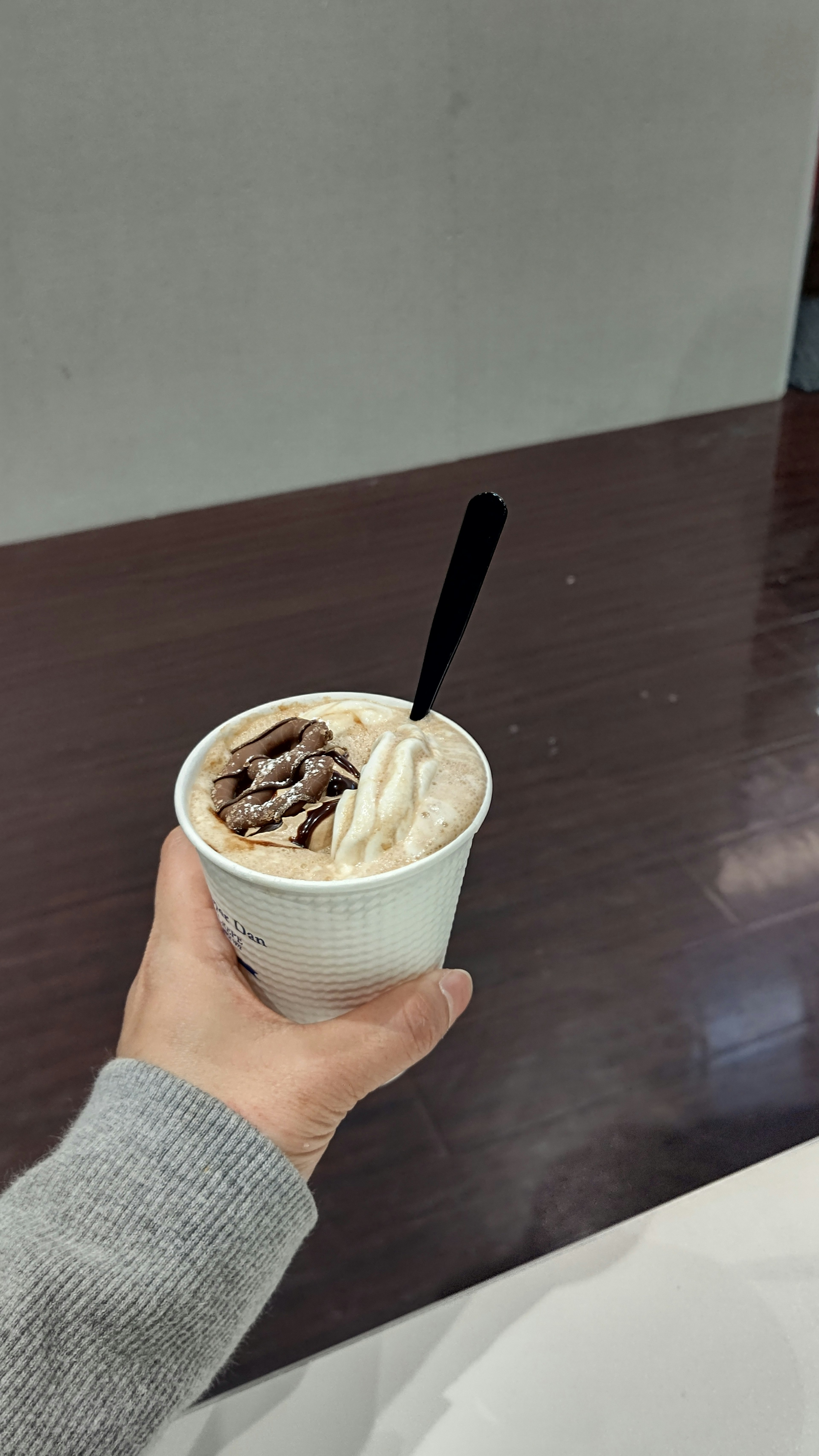 Hand holding a cup of ice cream with a black spoon on a wooden table